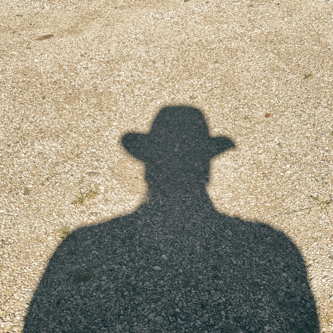 Shadow of a person wearing a hat on a sandy surface, symbolizing reflection and understanding.