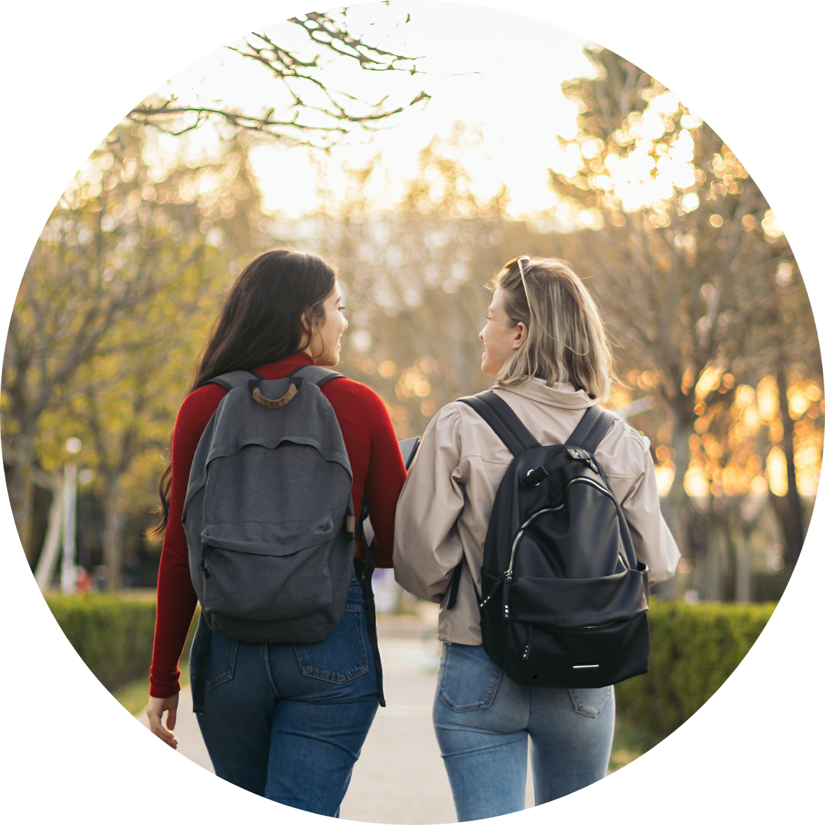 Two women with backpacks talking while walking outdoors in a park during sunset, symbolizing casual, yet  purposeful conversations.
