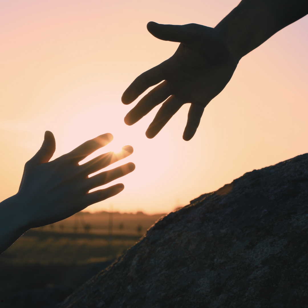 Two hands reaching towards each other with the sunset in the background - representing reaching for help.