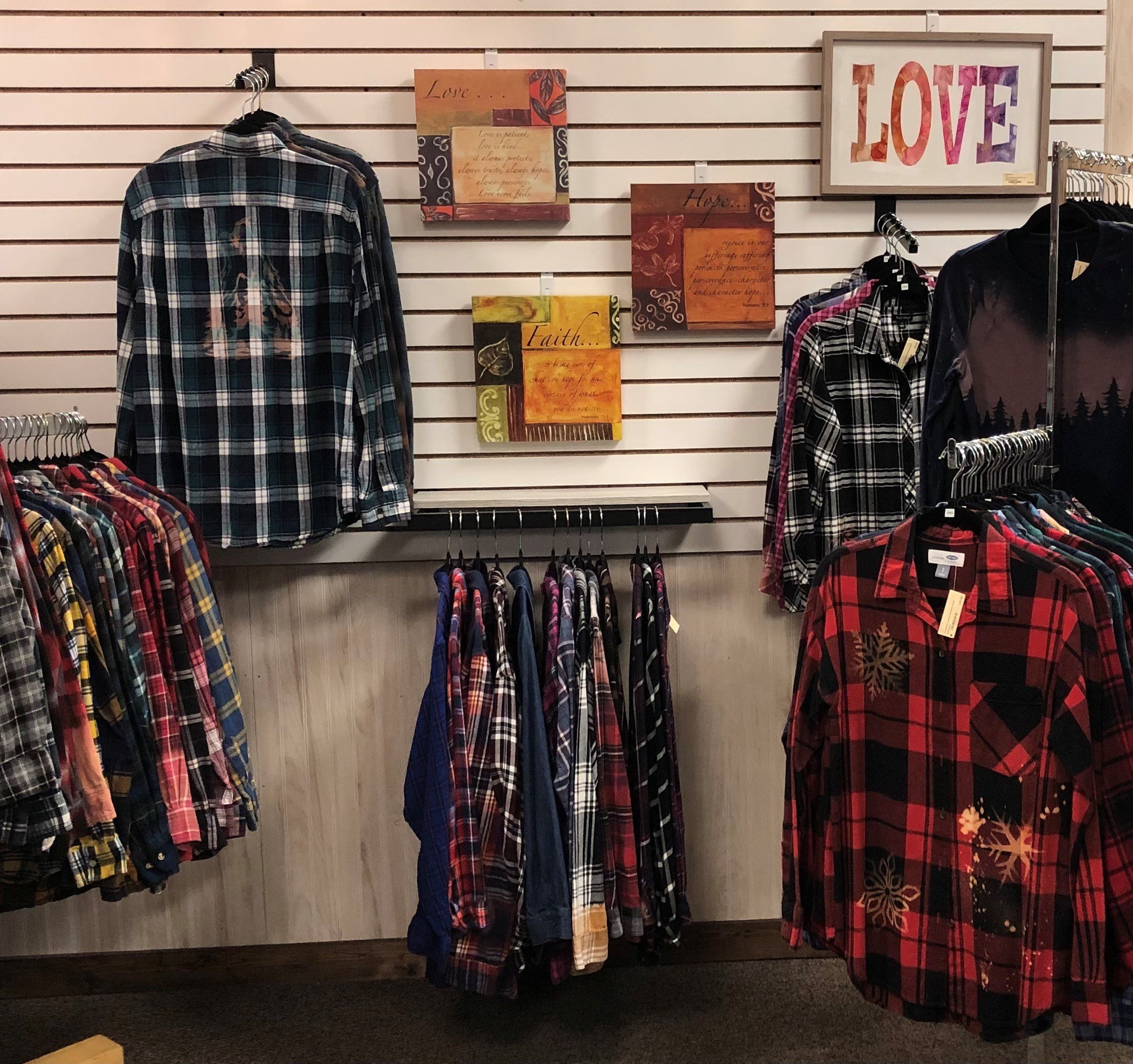 Display of plaid flannel shirts and Christmas decorations including a wreath, Santa hat, and holiday signs in a retail store.