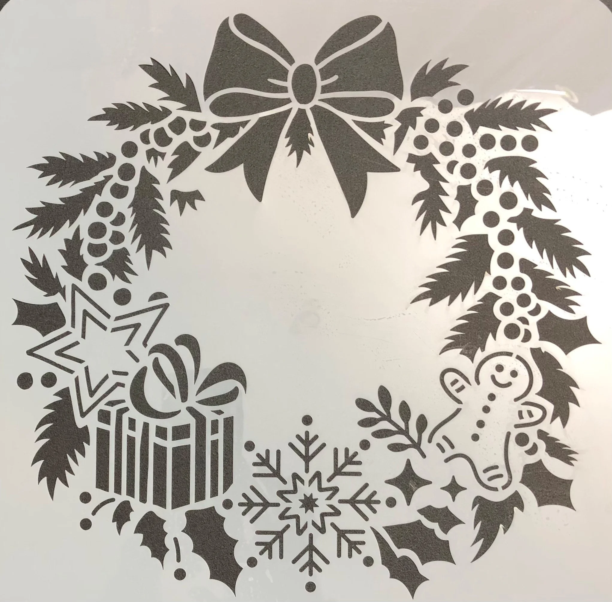 Black and white holiday wreath with a bow at the top, featuring holly leaves, berries, a gift box with a bow, a snowflake, a gingerbread man, and stars.
