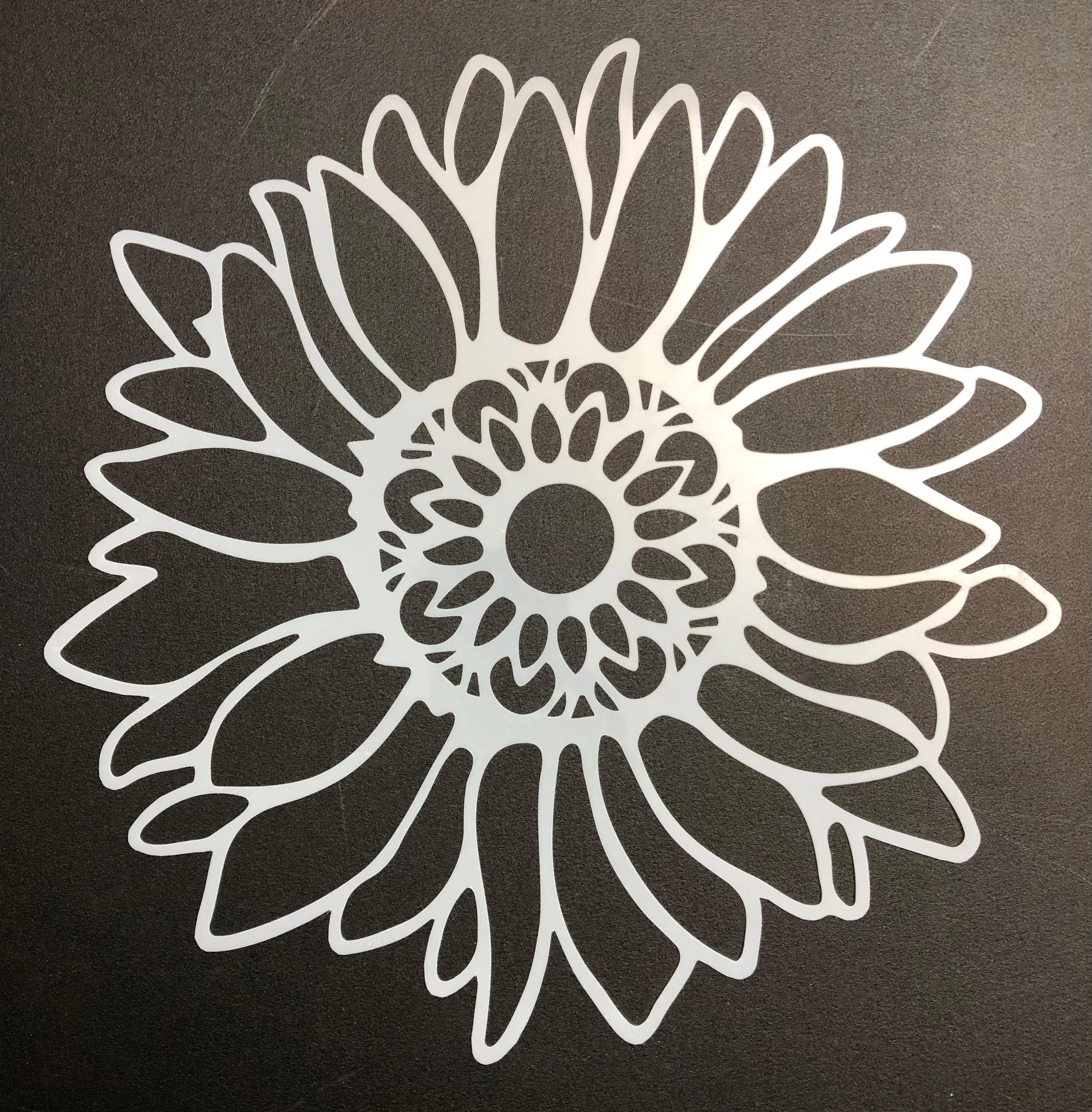 A white decorative paper cutout in the shape of a flower with multiple layers of petals on a dark background.
