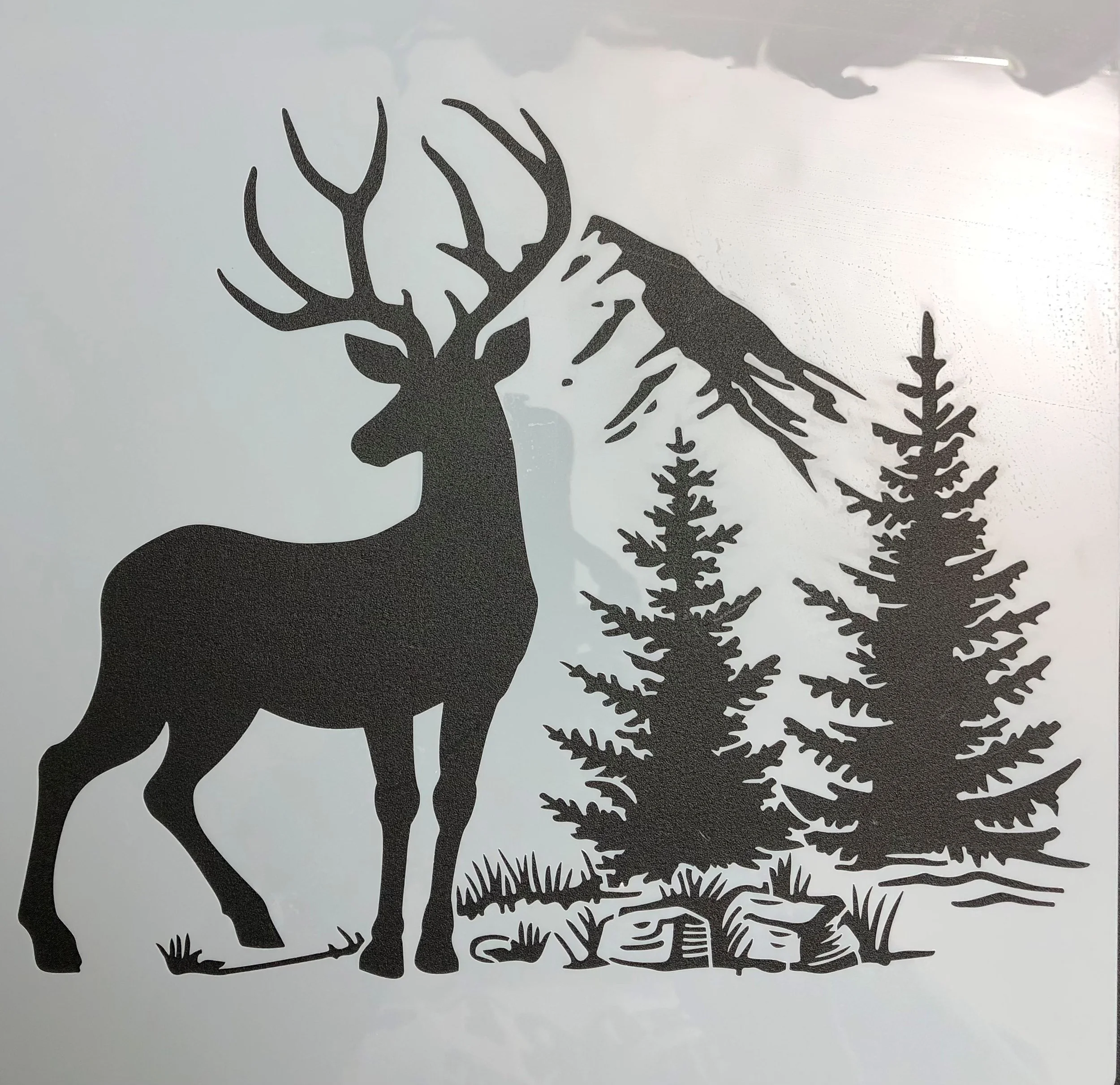 Silhouette of a deer with large antlers standing in front of pine trees and a mountain in the background.