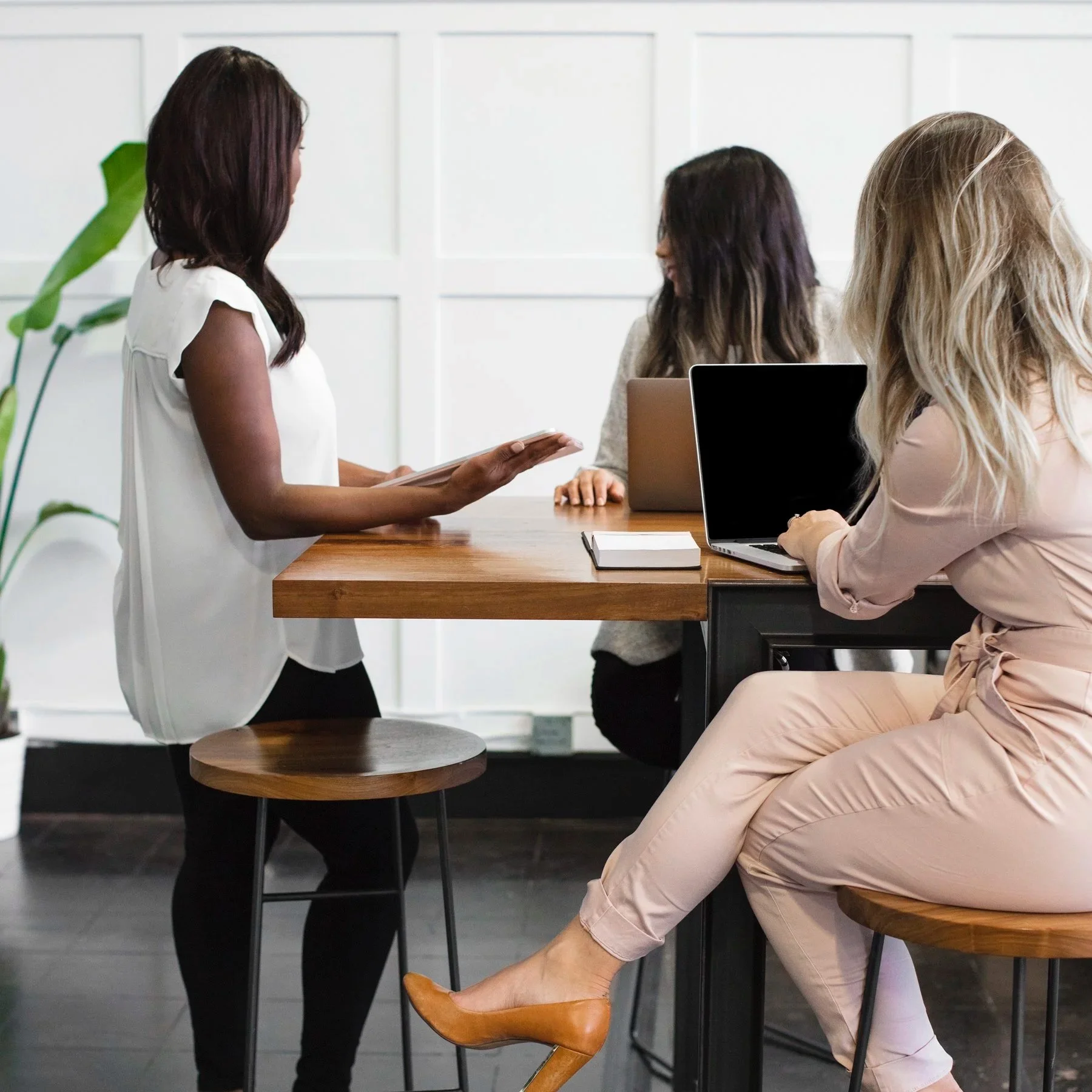High performing women leaders in a business meeting or discussion in an office, with laptops and notebooks on the table.