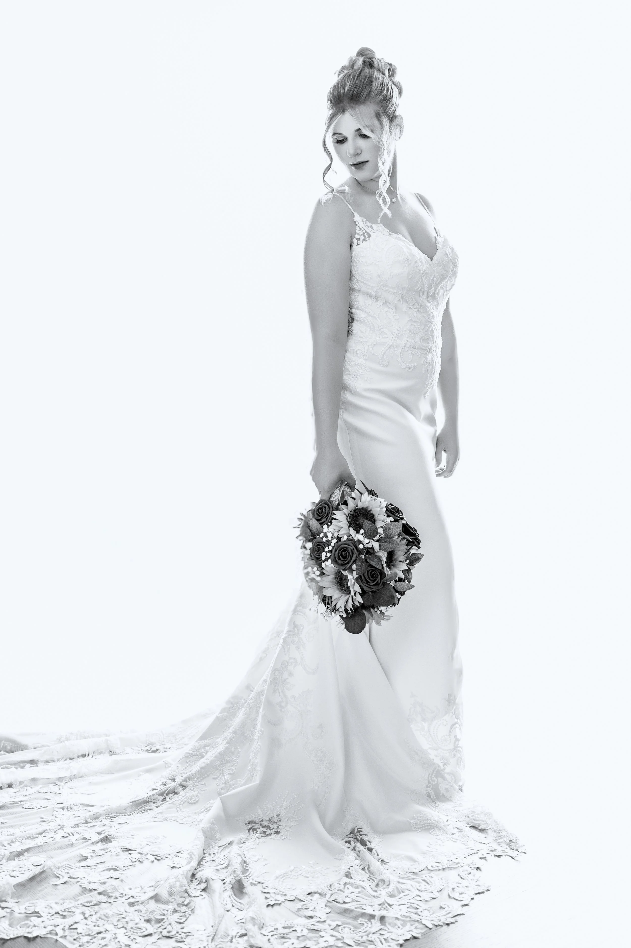 A bride in a white wedding dress is holding a bouquet of flowers in a studio setting with a plain light background.