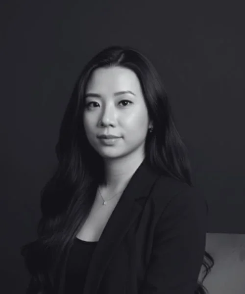 Black and white portrait of a woman with long dark hair, wearing a blazer and looking at the camera.