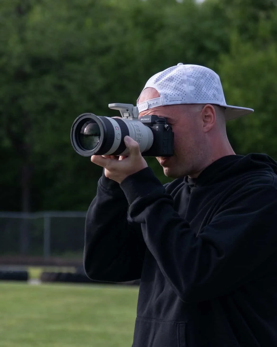 Gavin Gill, owner of Gavin (Bison) Media, taking a photograph with a professional camera outdoors, with trees and a field in the background.