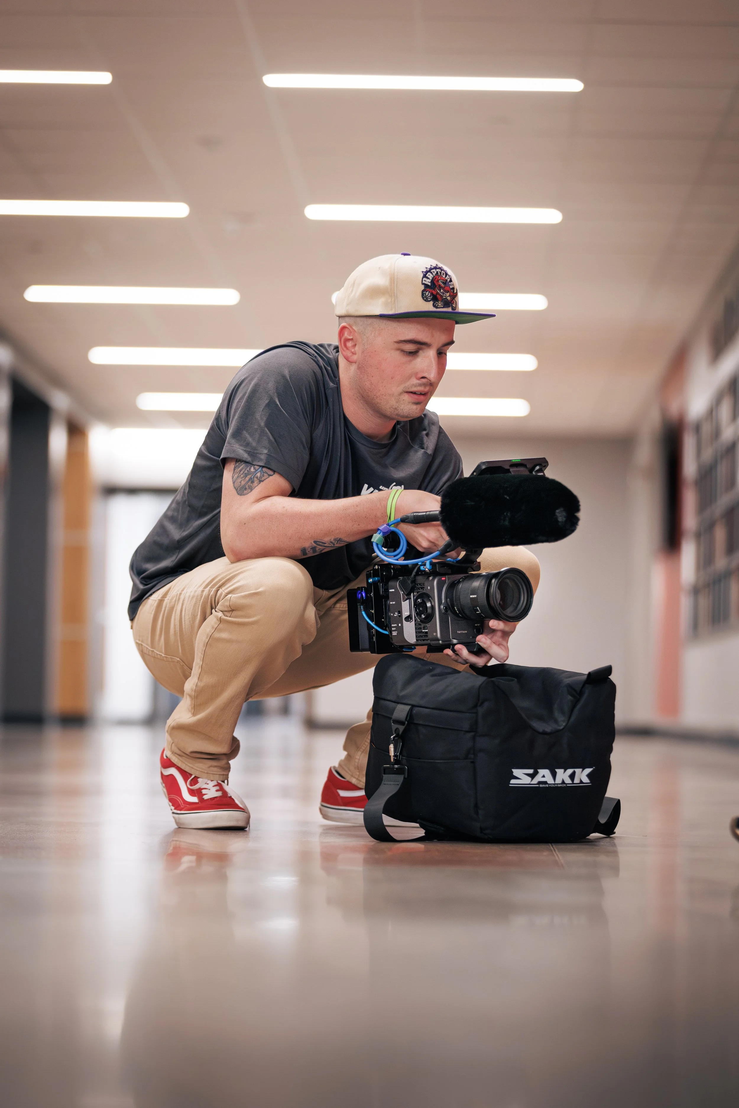 Videographer from Gavin (Bison) Videos crouched in a hallway rigging a cinema camera next to a gear bag.”