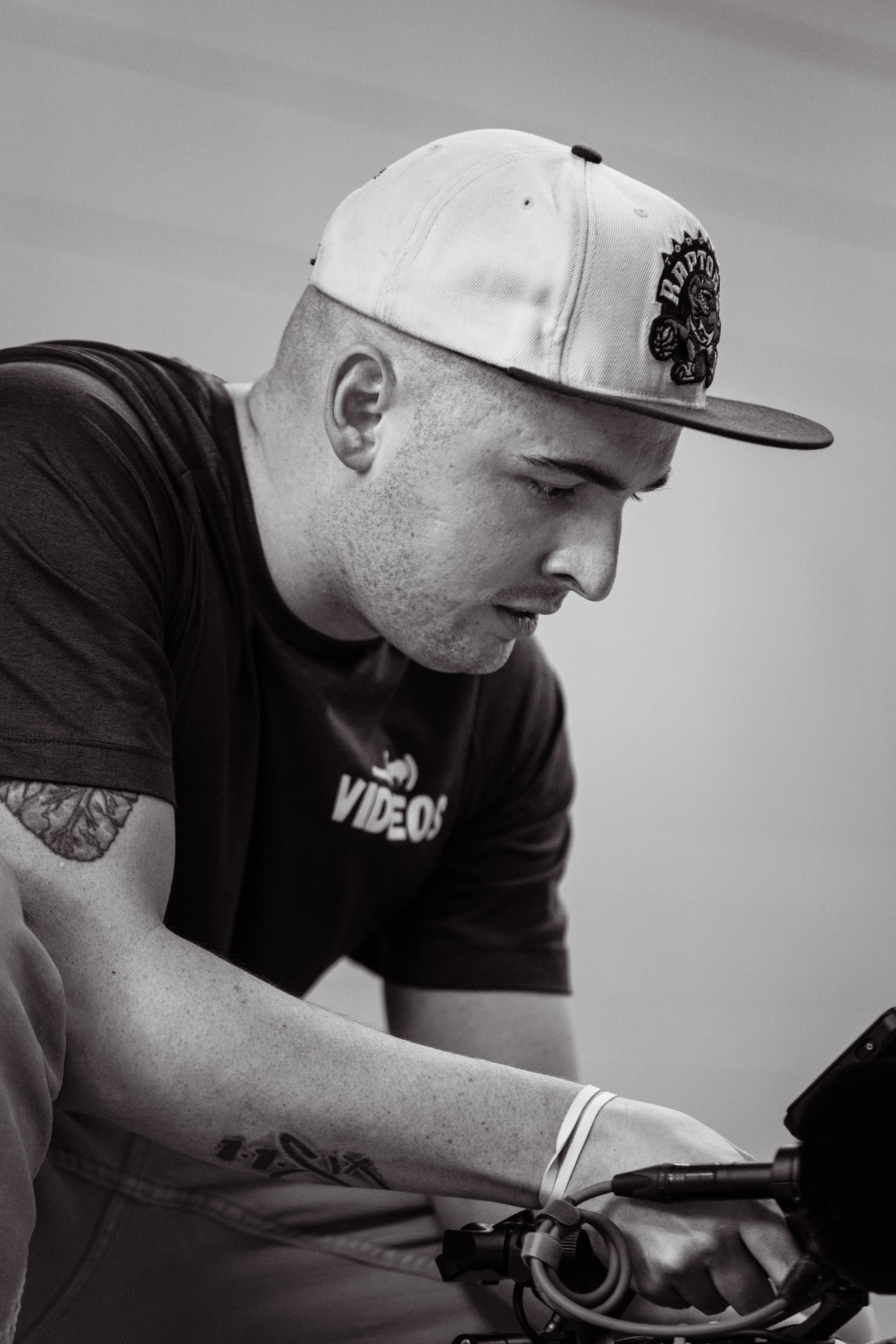 A videographer from Gavin (Bison) Videos wearing a white Toronto Raptors cap and a black T-shirt, focused on working with a Sony FX6 on a production set.
