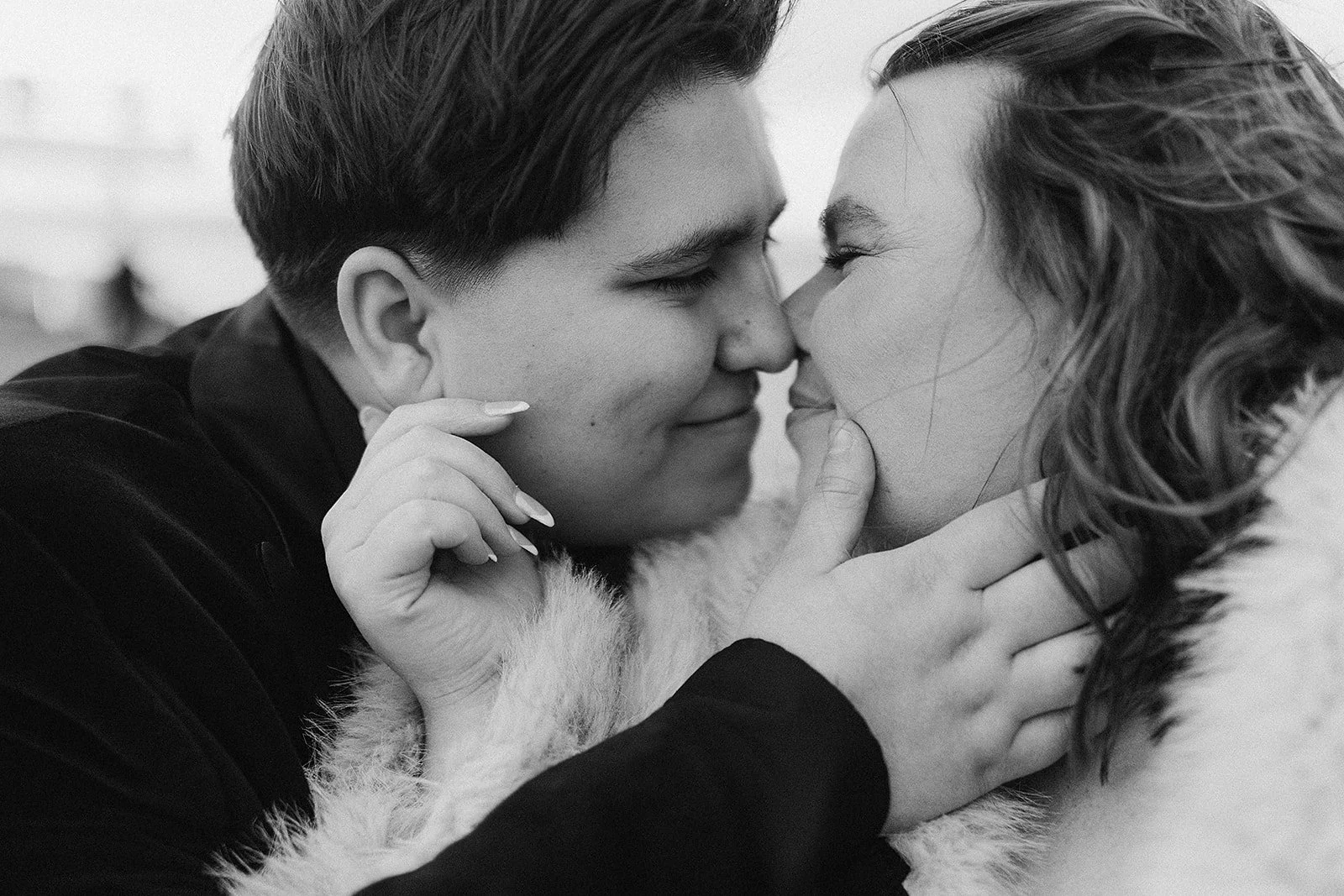 A black and white close-up photo of a couple touching noses and smiling, with one person gently holding the other's face