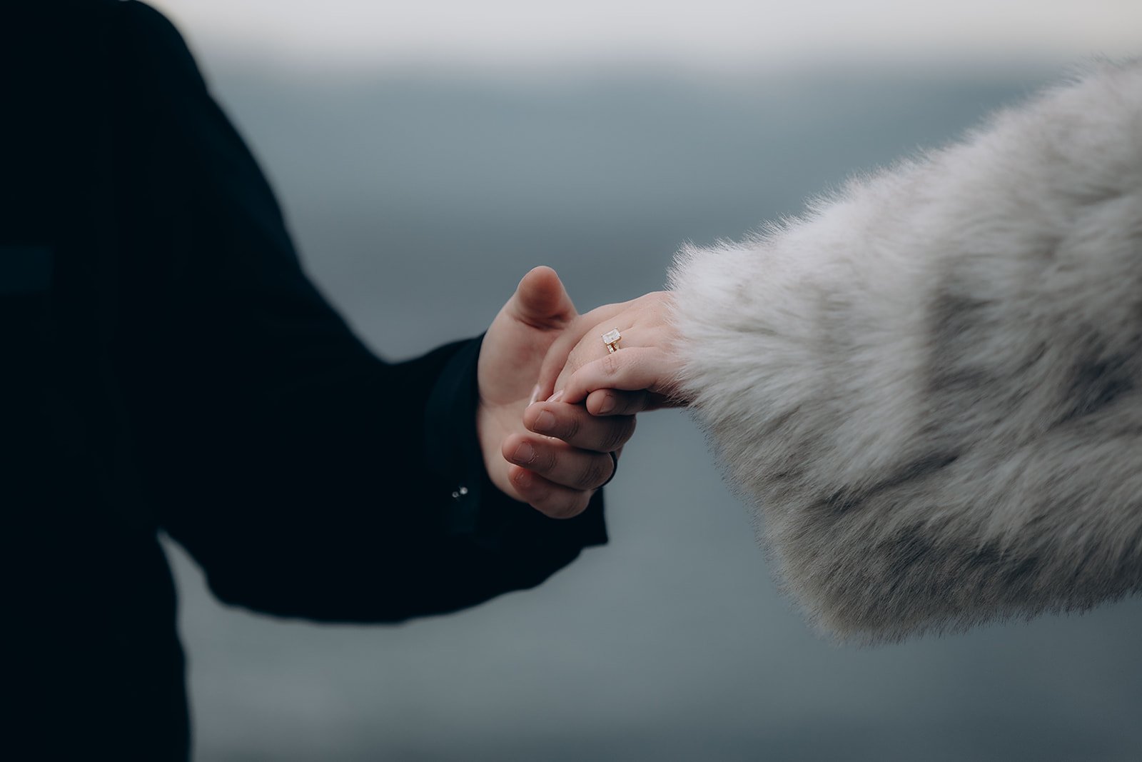 A person wearing a dark jacket reaches for another person's hand, wearing a fur coat.