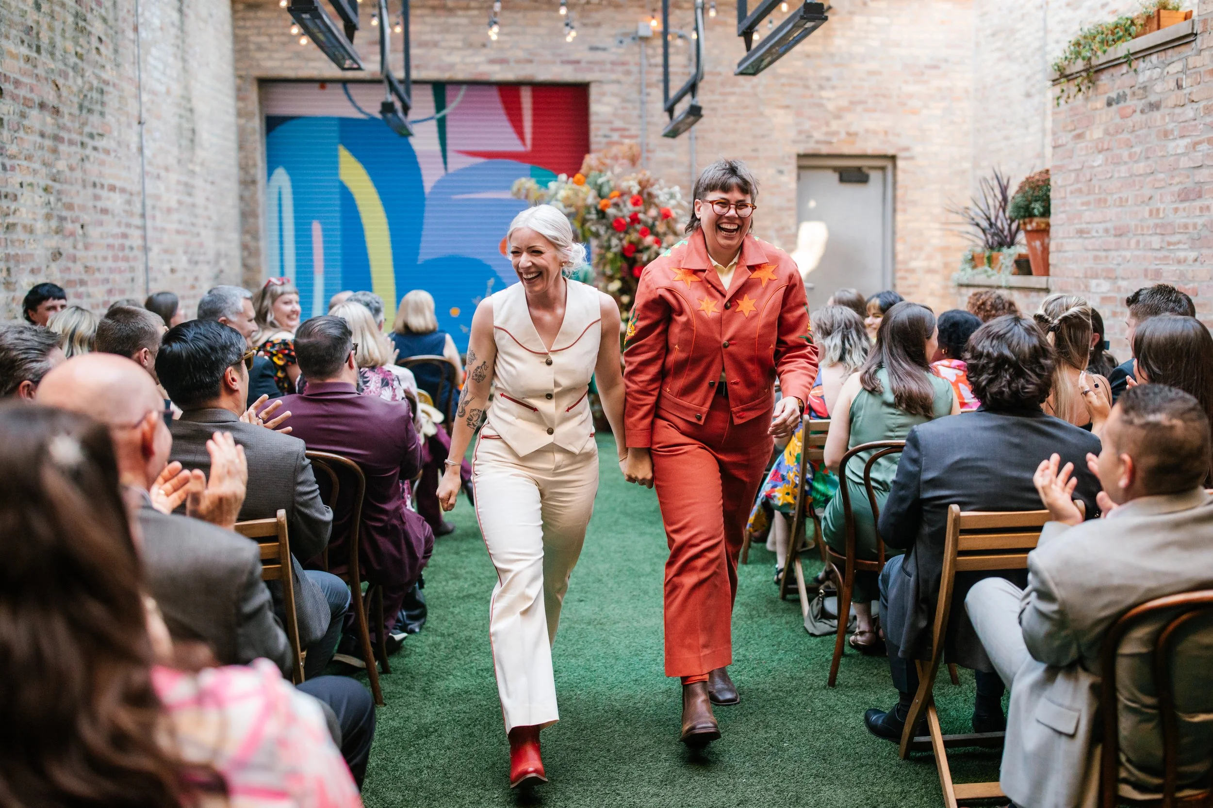 two women walk down the aisle while their guests cheer for them