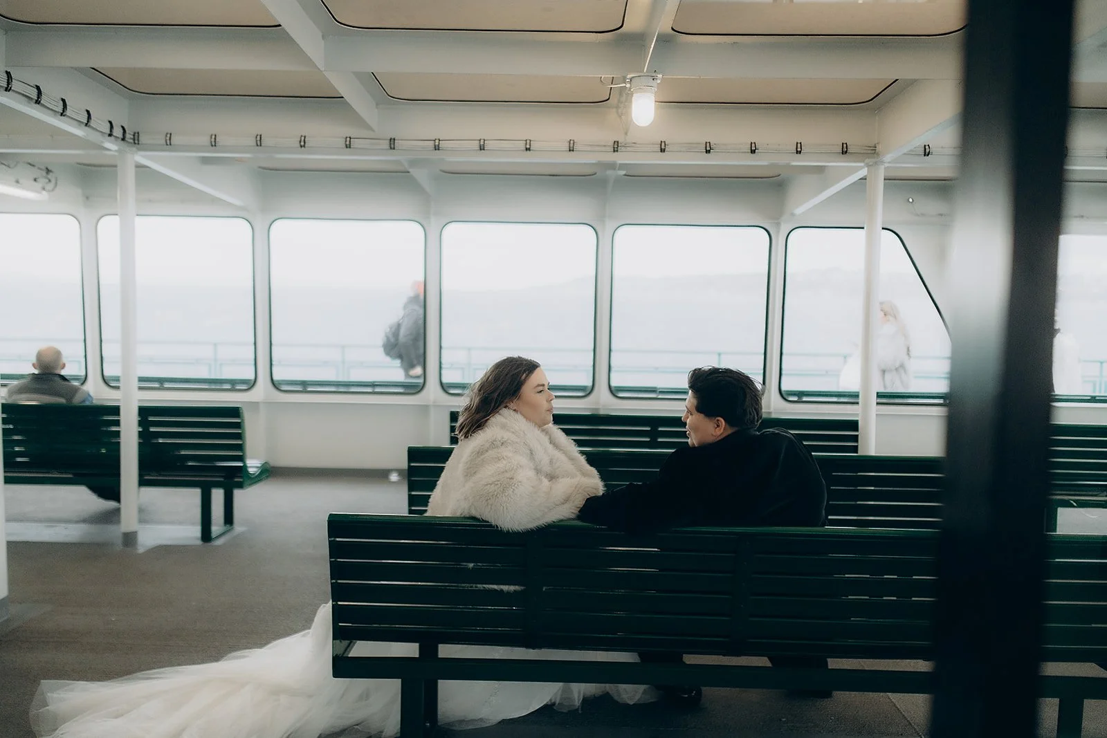 A couple sitting on a bench inside a ferry, dressed in formal attire.