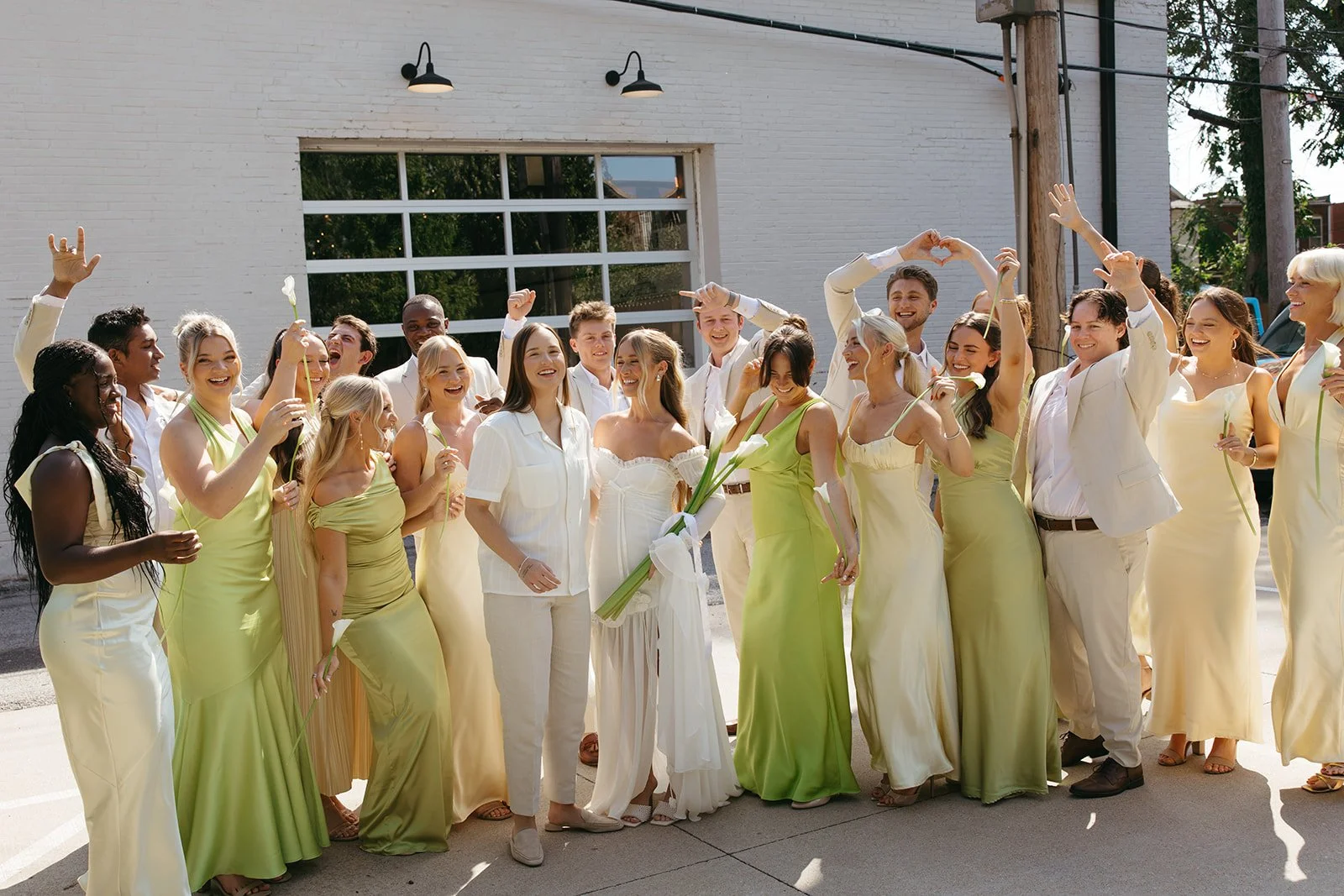 a wedding party in matching green and yellow outfits lift their arms and cheer for the two brides