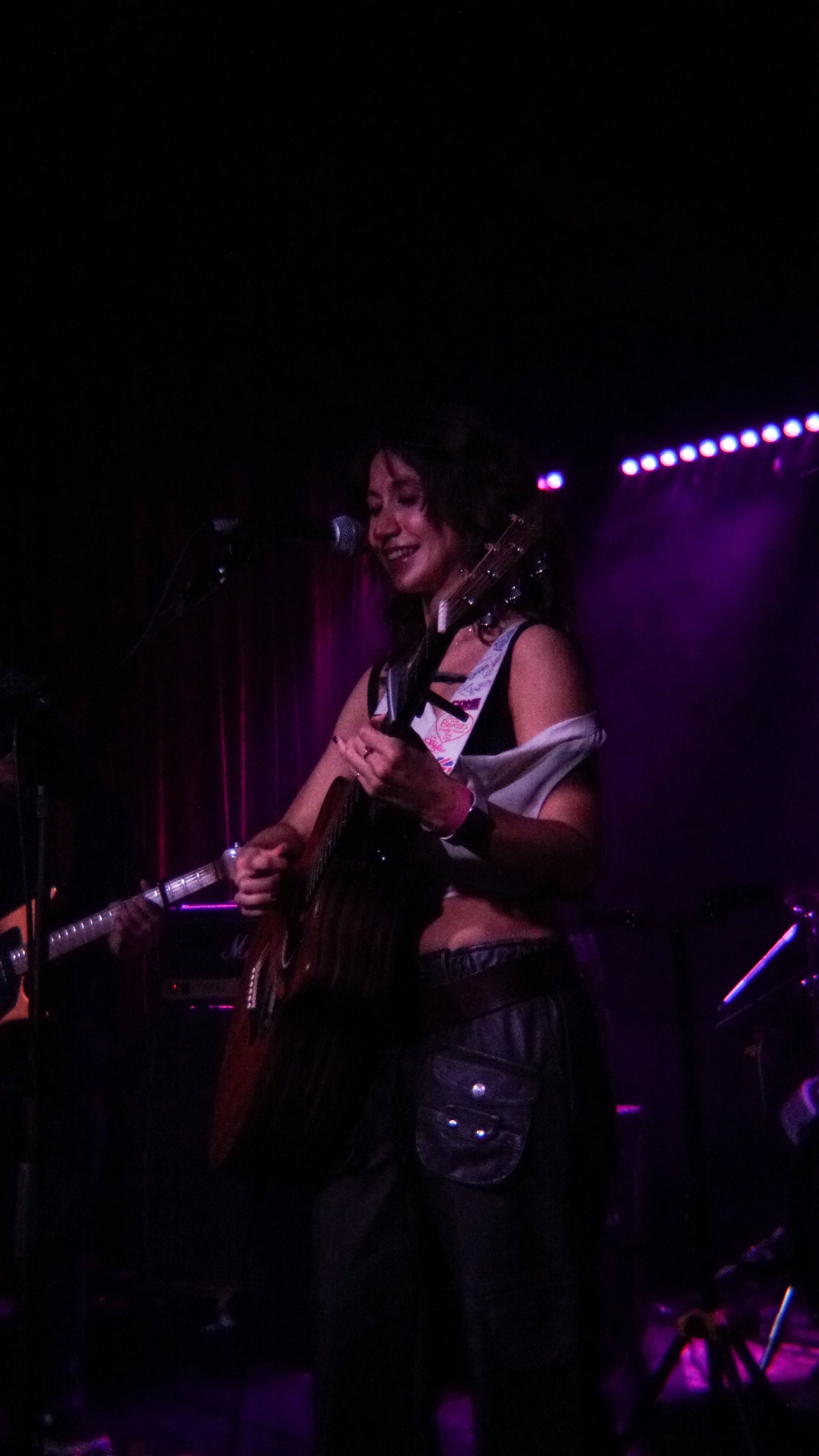 A woman playing an acoustic guitar and singing on stage with purple lighting.