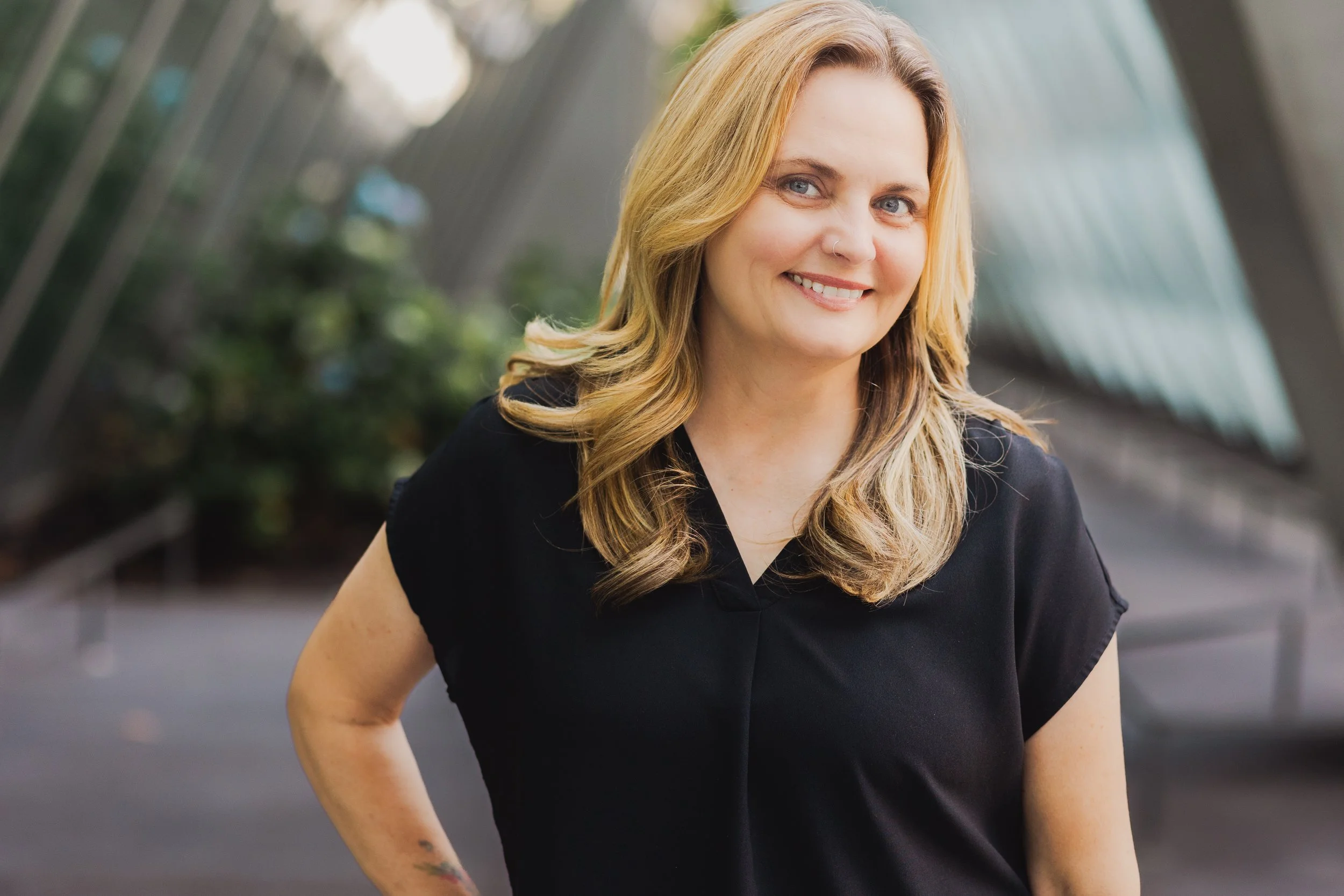 Professional outdoor branding portrait of author and life coach Debra Bryant smiling in front of a modern architectural backdrop.
