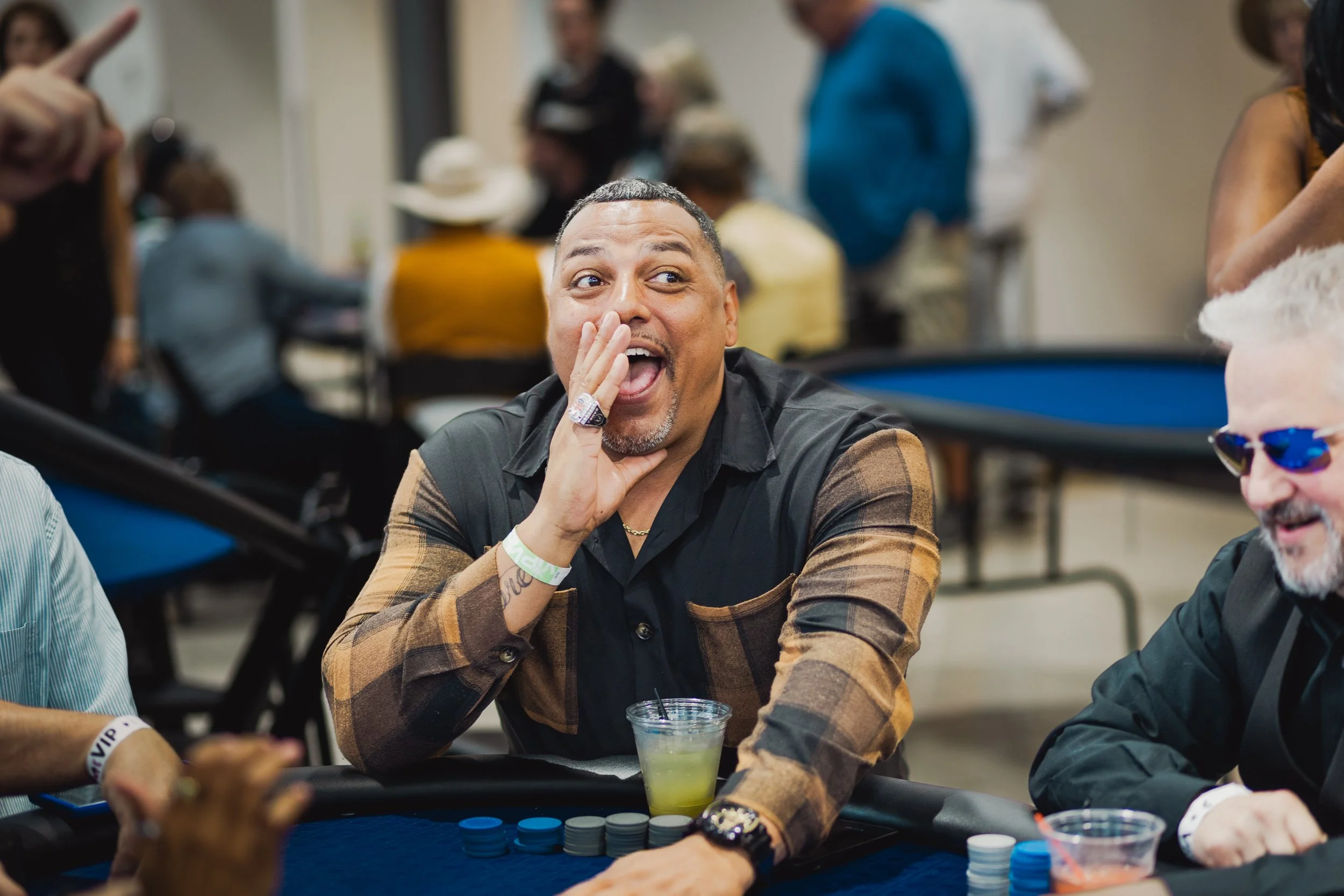 Gerald Smiley smiles and gestures across a poker table during a lively charity casino event, with poker chips and other guests in the background.