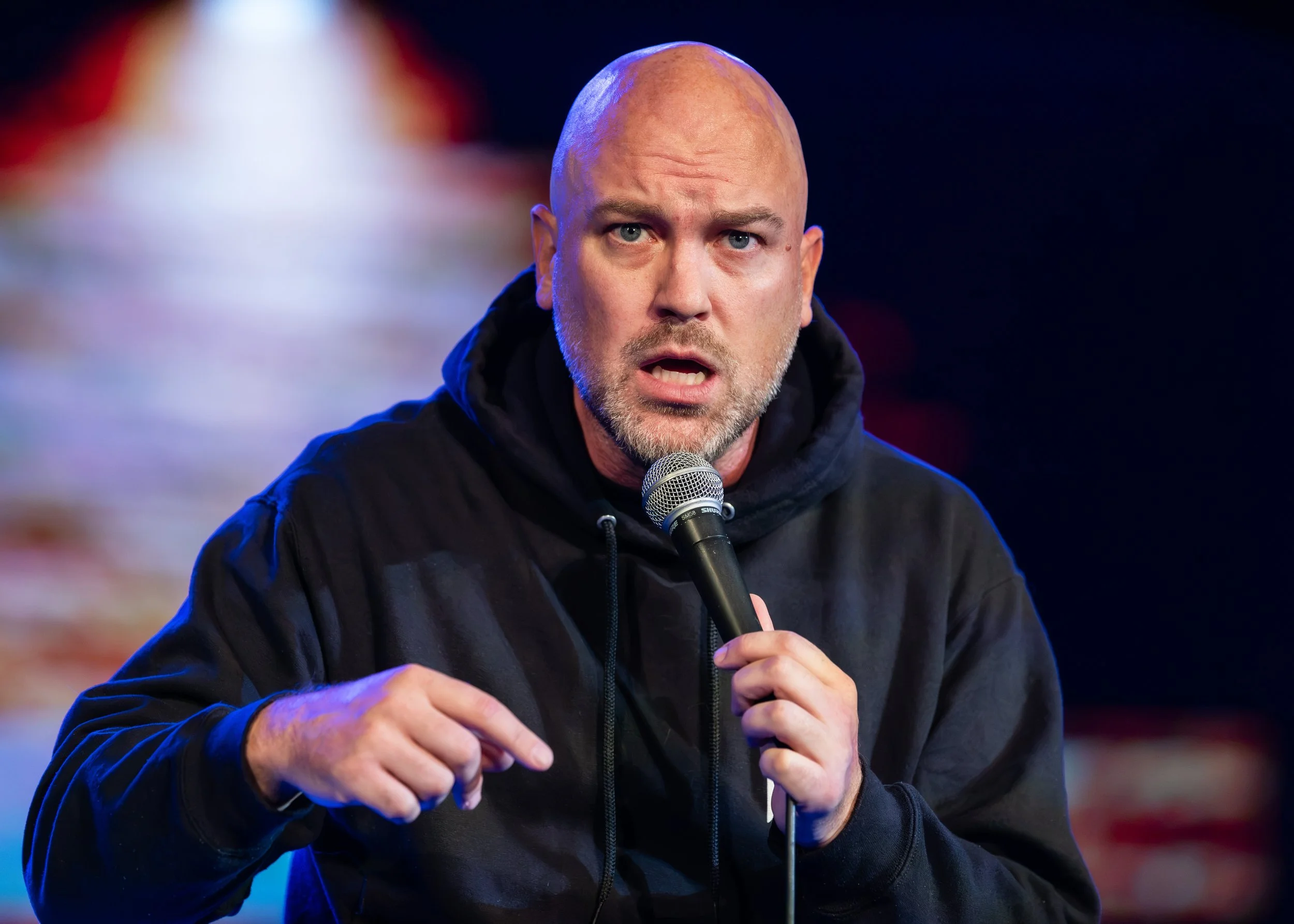 Cory Michaelis flashes his bright blue eyes on stage at the new everett theater, hosting everett comedy wearing his brad upton branded sweatshirt merchandise