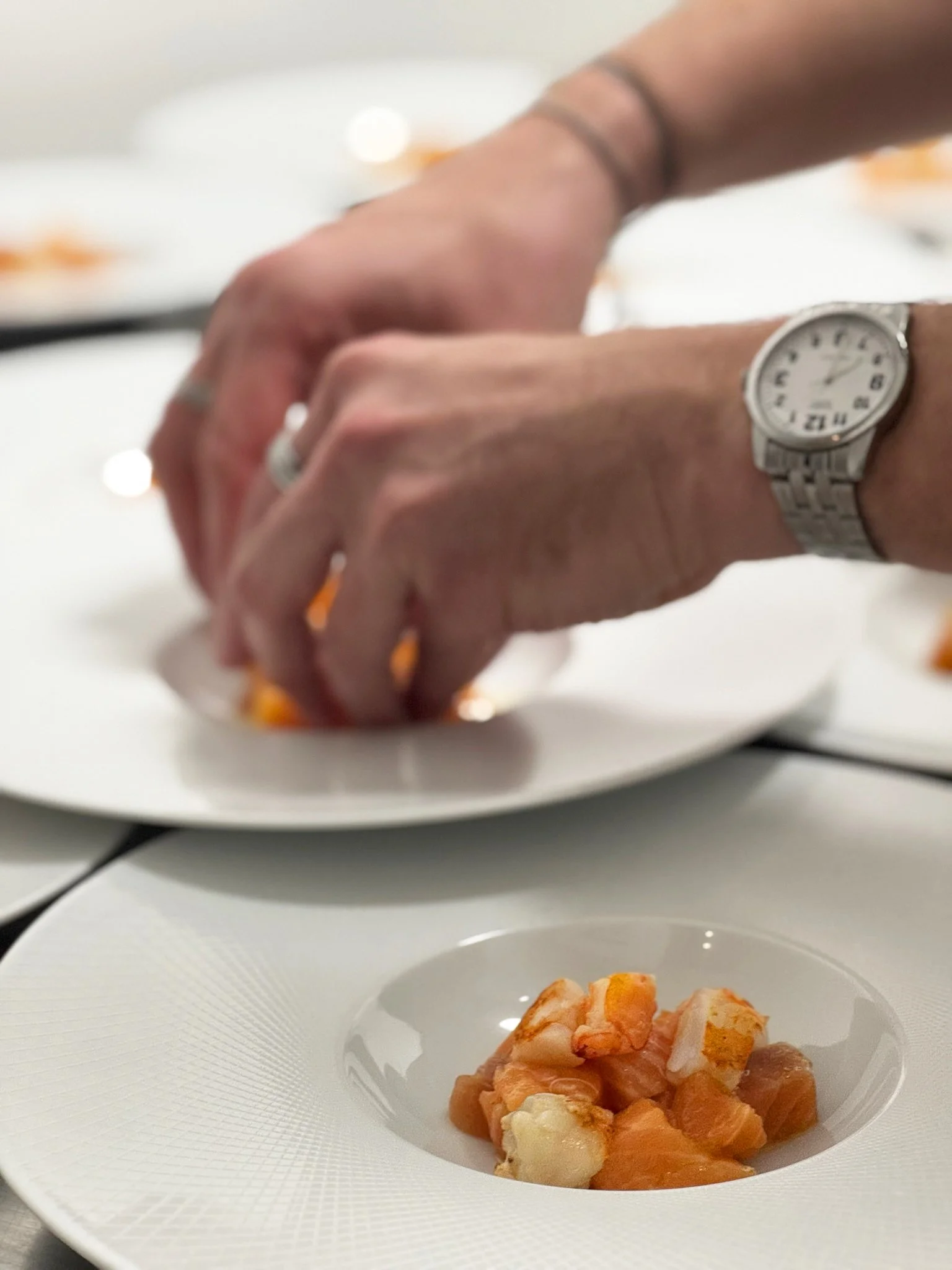 Une main ajustant une assiette avec un plat de petits morceaux de poisson ou de fruit de mer dans un environnement de cuisine ou de service de restauration.