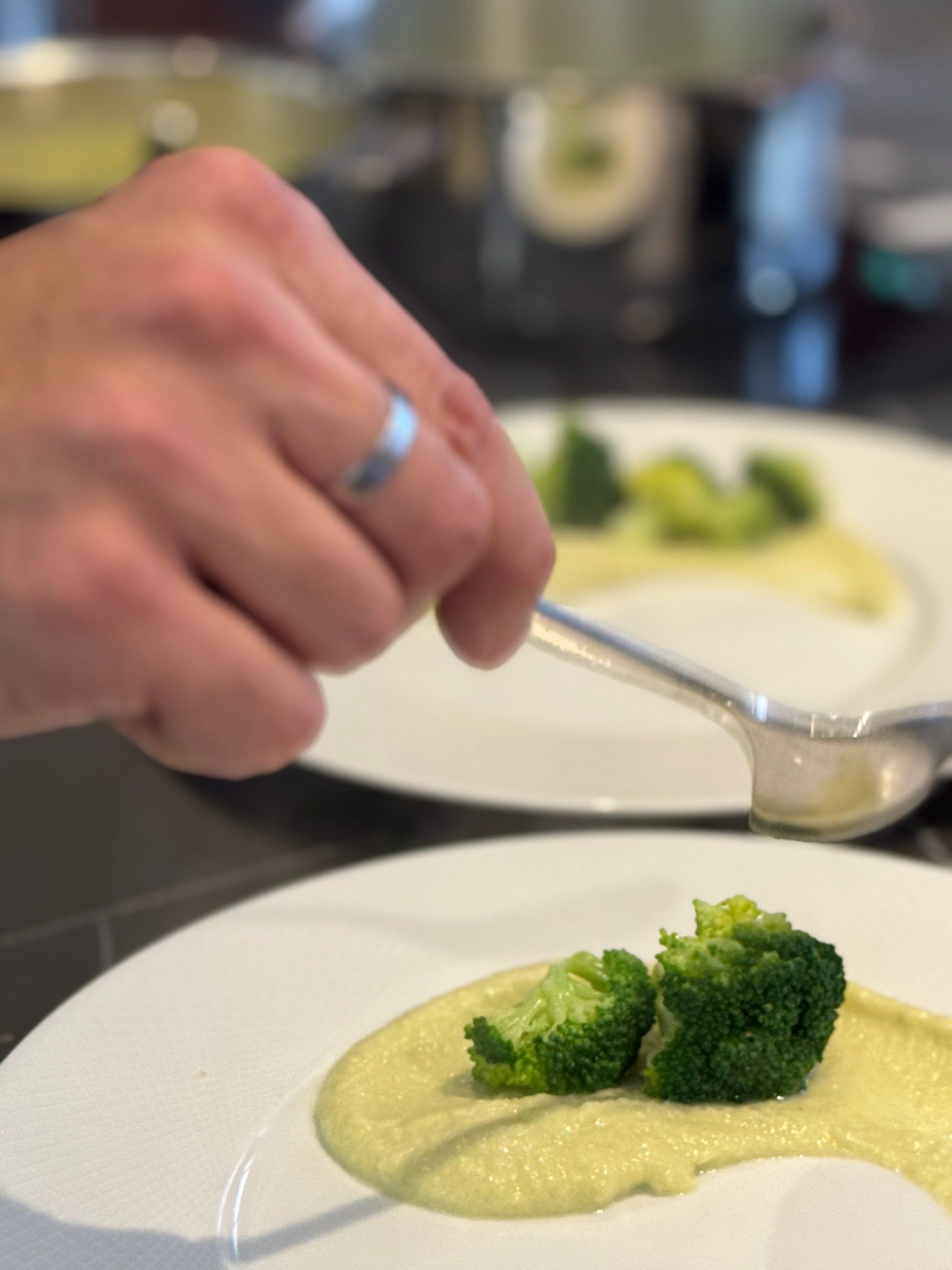 Une main en train de verser une sauce sur une assiette contenant du brocoli.