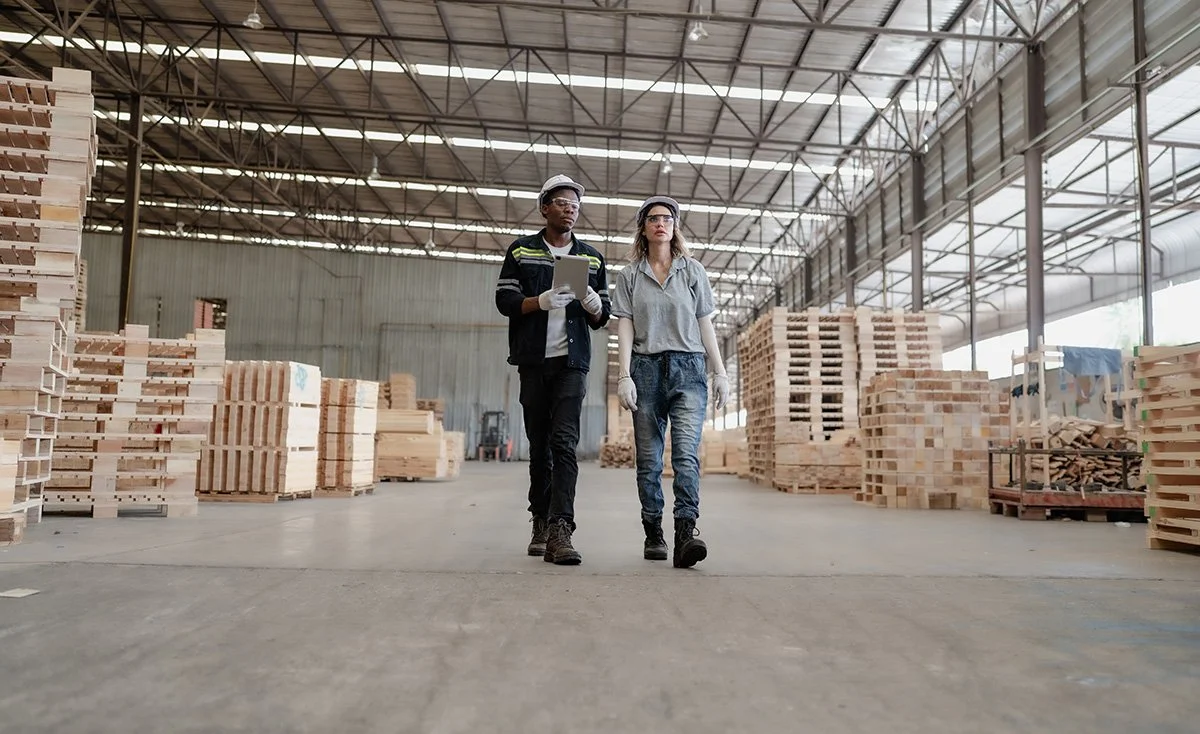Two workers walking through a warehouse with stacks of pallets in the background
