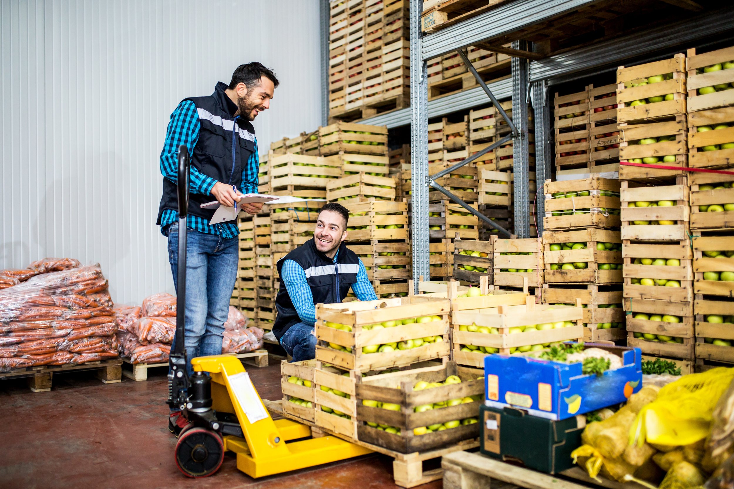 Two workers next to a section of food pallets filled with apples in a warehouse