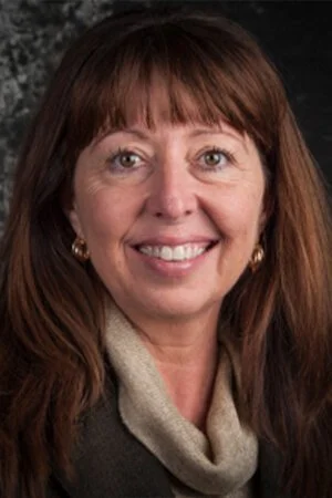 Portrait of a woman with brown hair and a beige scarf, smiling.