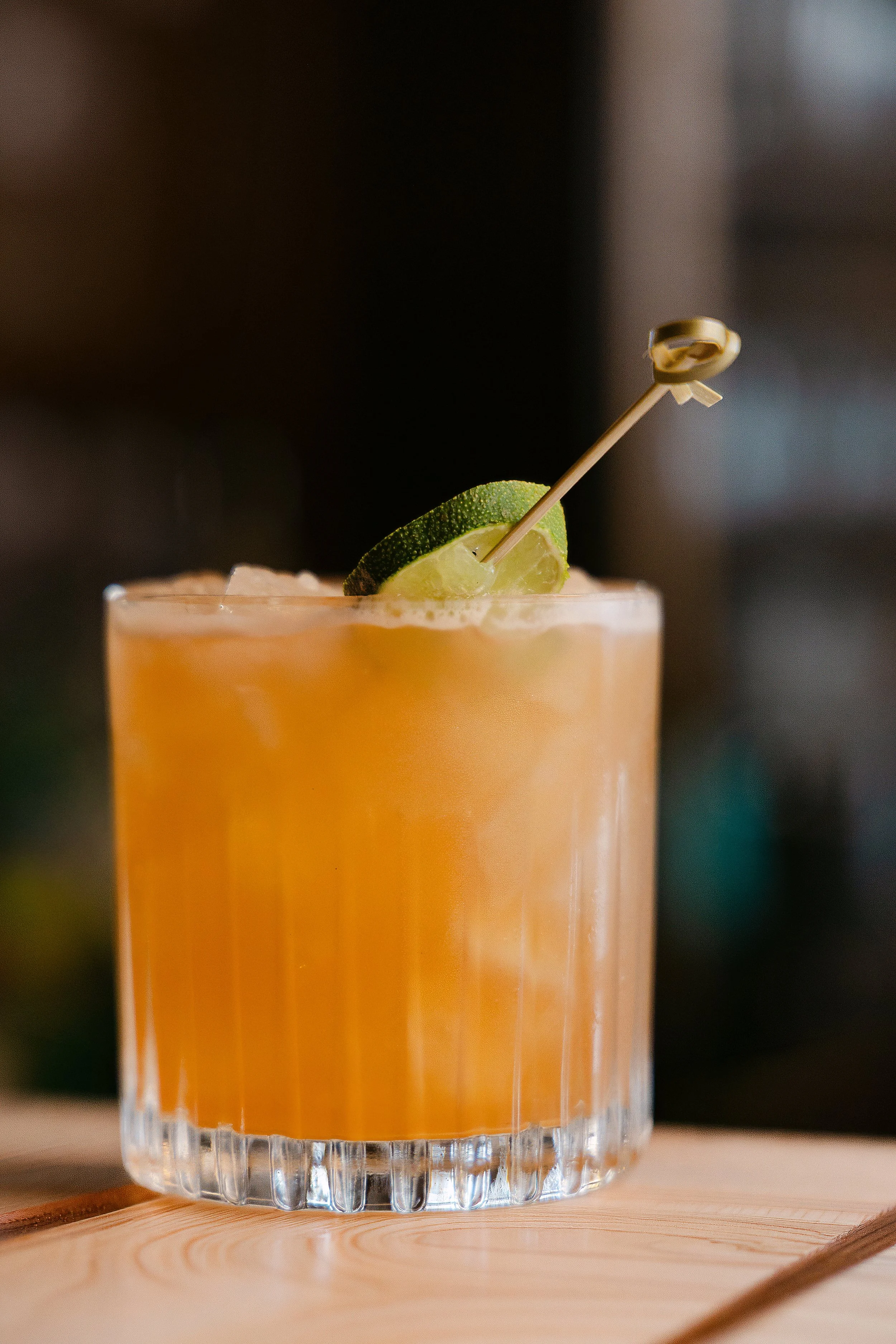 A cocktail drink in a clear glass with lime garnished with a small lime wedge and a decorative pick.