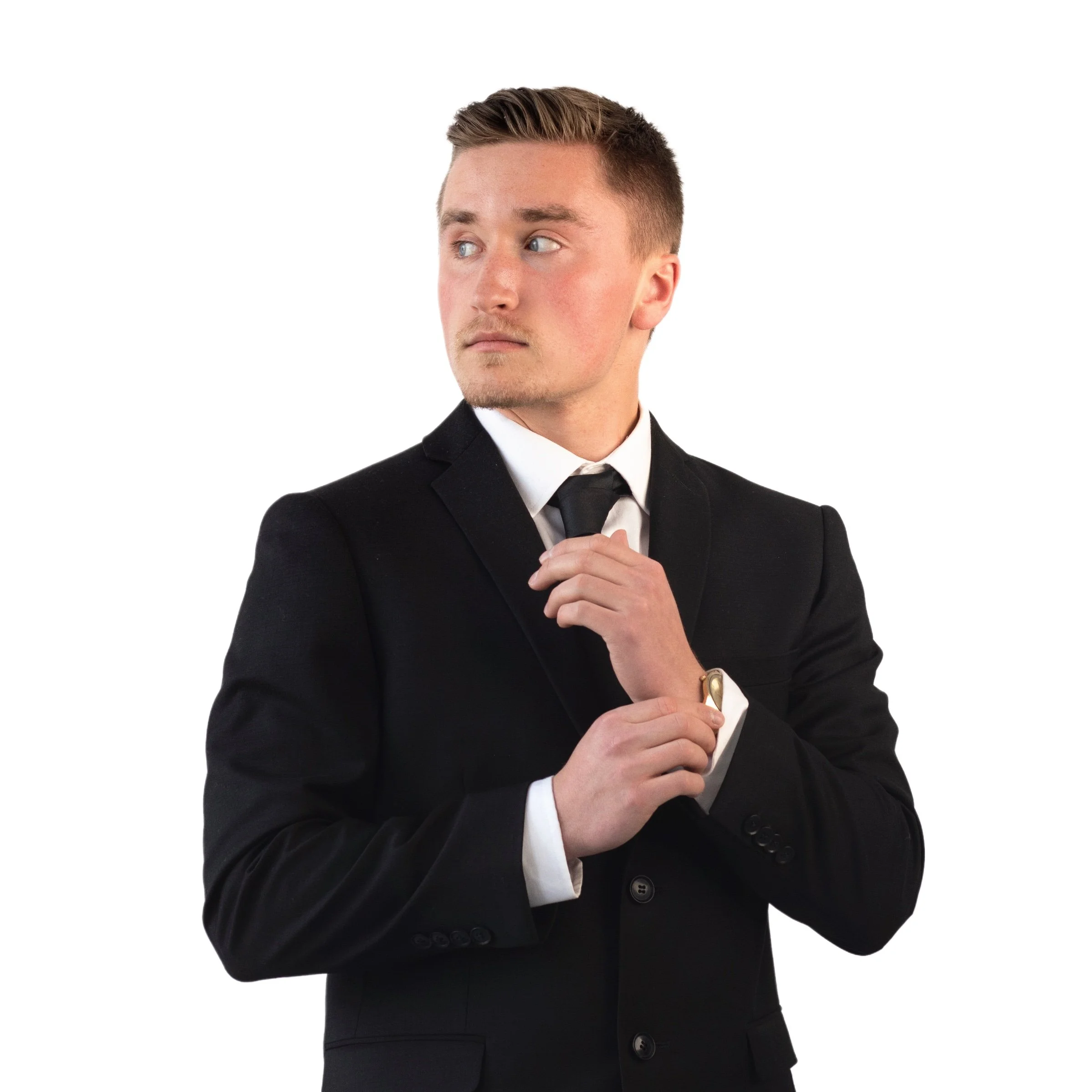 Young man in a black suit adjusting his tie against a white background.