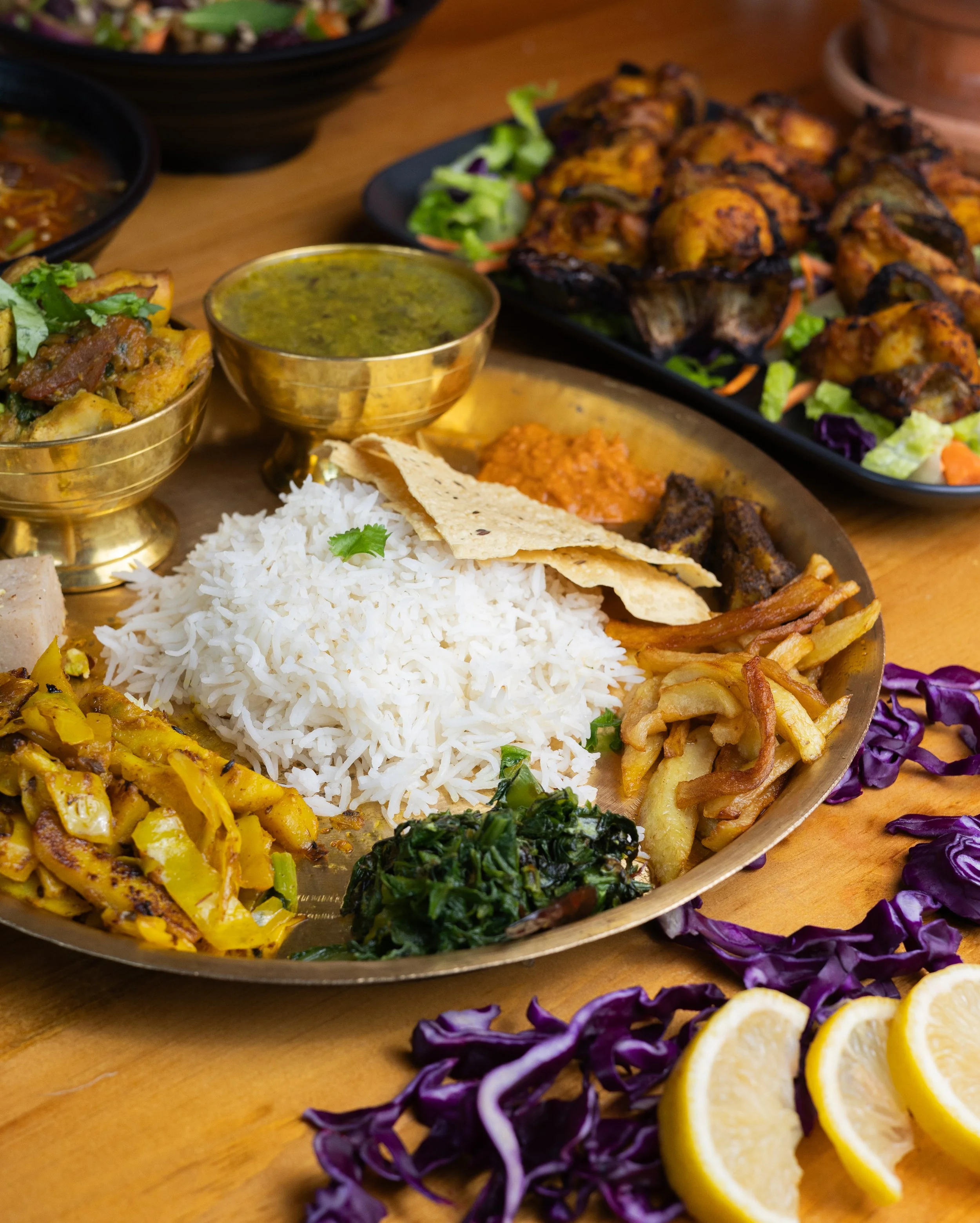 Indian thali with white rice, naan bread, various vegetable dishes, and two small bowls of curry, garnished with lemon slices and purple cabbage.