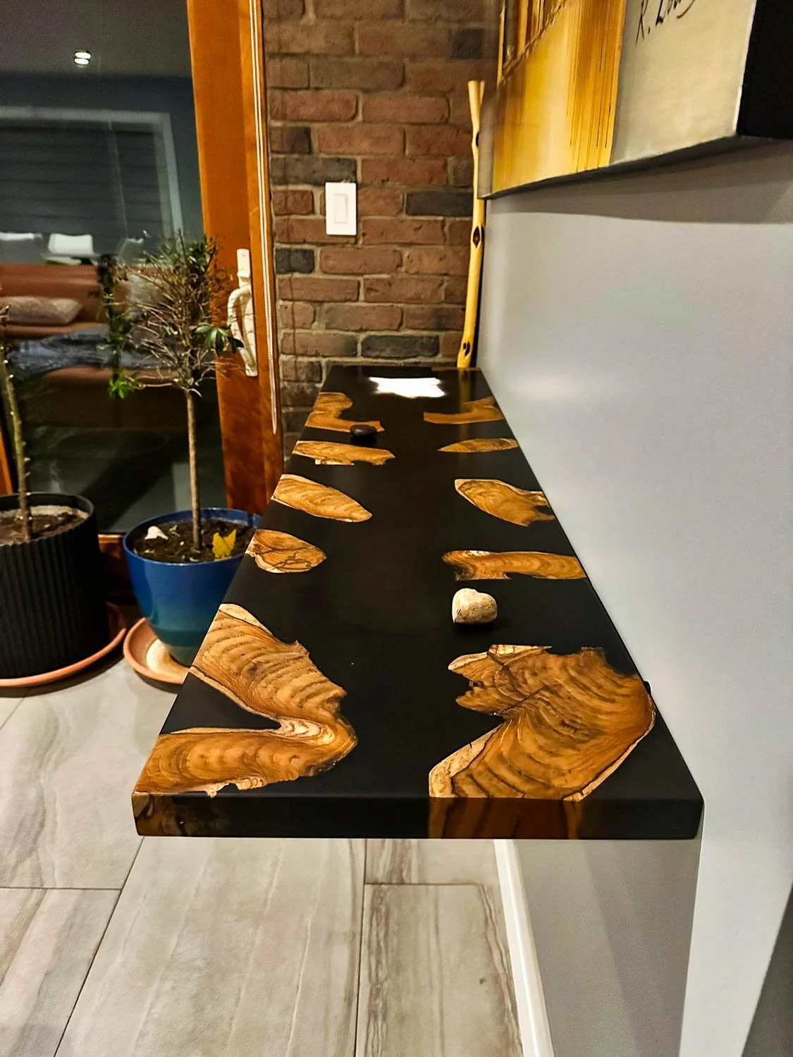 Wooden table with a black surface and irregularly shaped wood inlays, situated against a white wall.