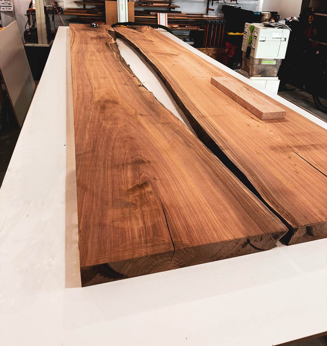 Large wooden slab with natural edge on a white workbench in a woodworking shop.