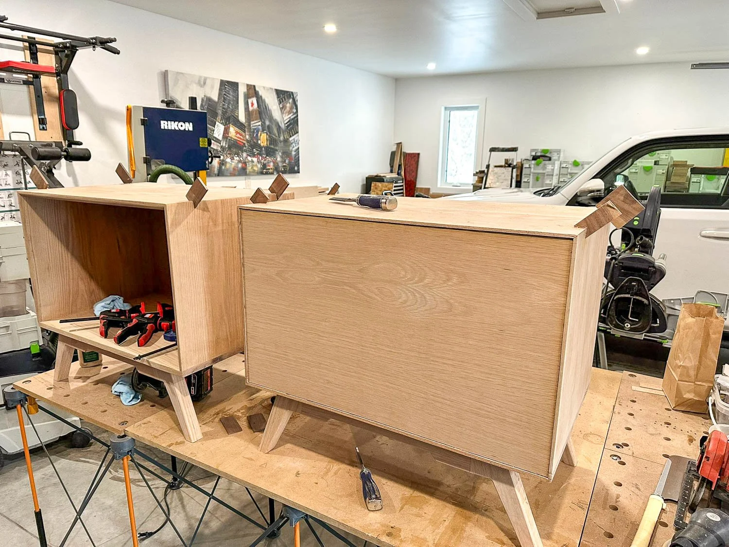 Unfinished wooden cabinets in a woodworking workshop with tools and equipment.