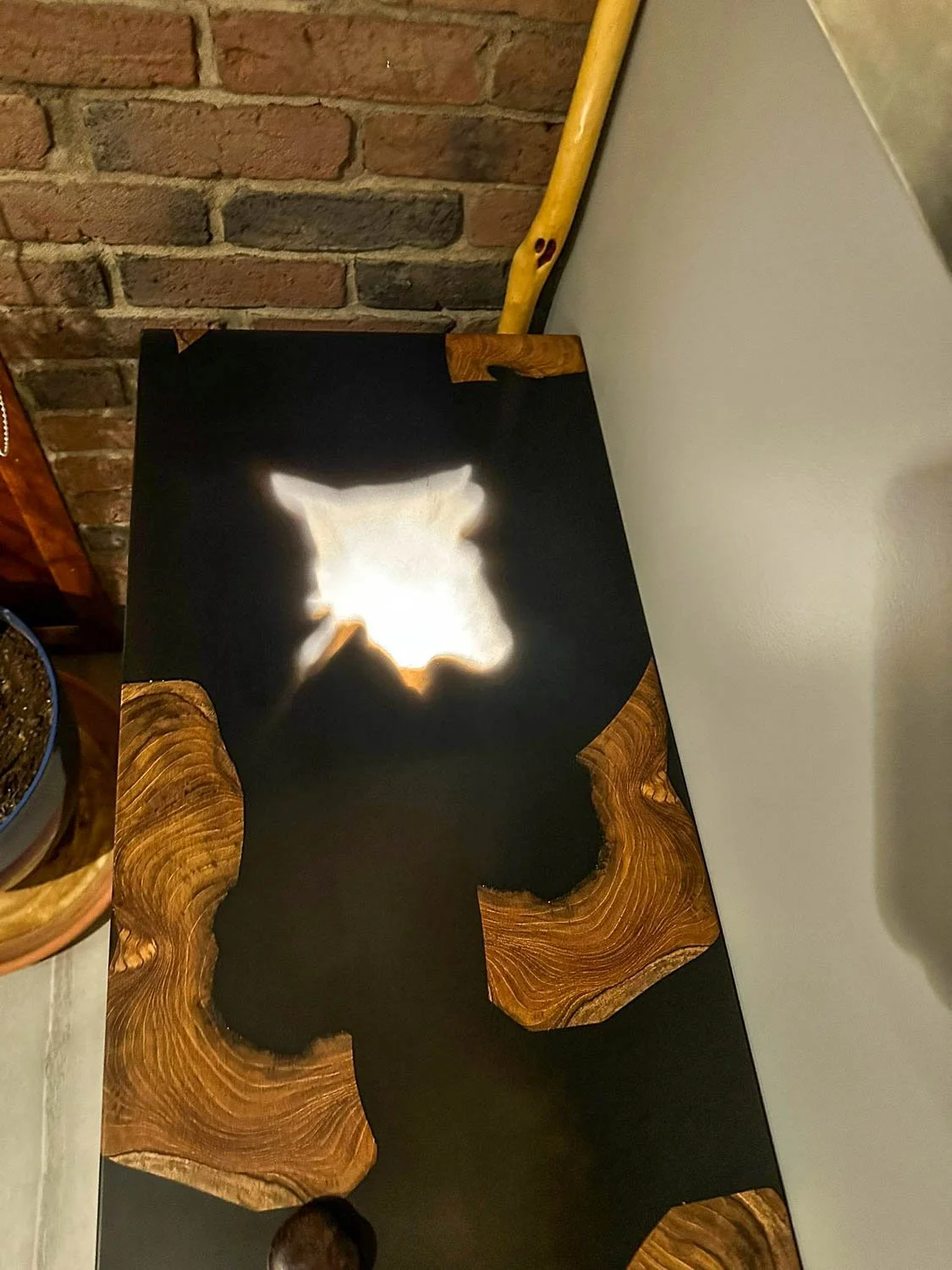 Wooden table with a star-shaped light reflection on top, against a brick wall background.