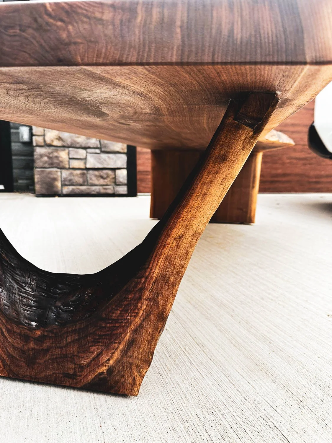 Close-up of a wooden furniture leg with a natural finish, showing the grain and design details, on a light-colored carpeted floor.