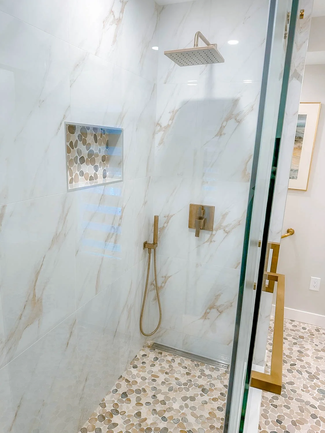 Modern walk-in shower with marble tiles, a large square showerhead, a built-in niche with pebble tile inside, and a handheld shower.