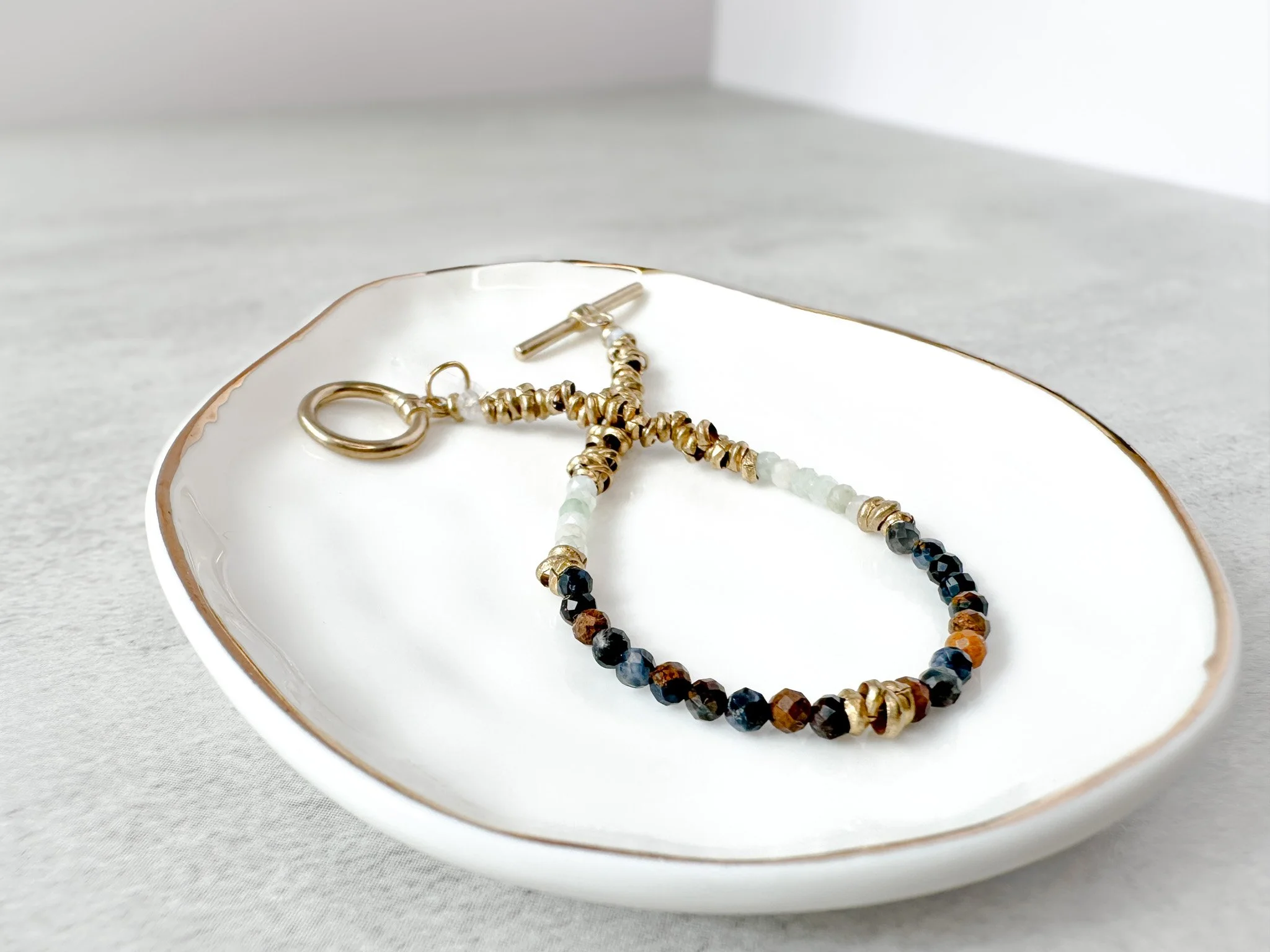 Tempest bracelet on dish with brass toggle clasp and clear quartz charm detail