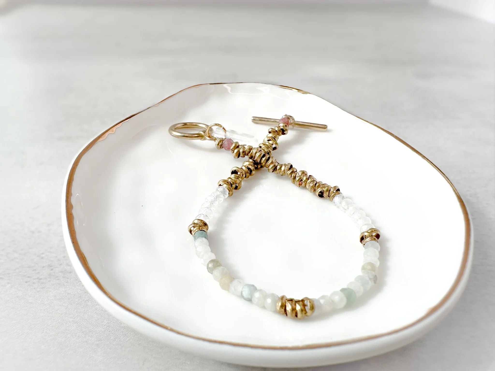 Eden bracelet on dish with brass toggle clasp and clear quartz charm detail