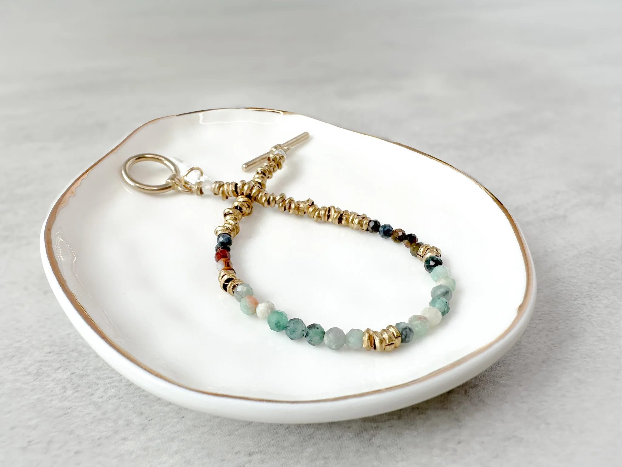 Aether bracelet on dish with brass toggle clasp and clear quartz charm detail