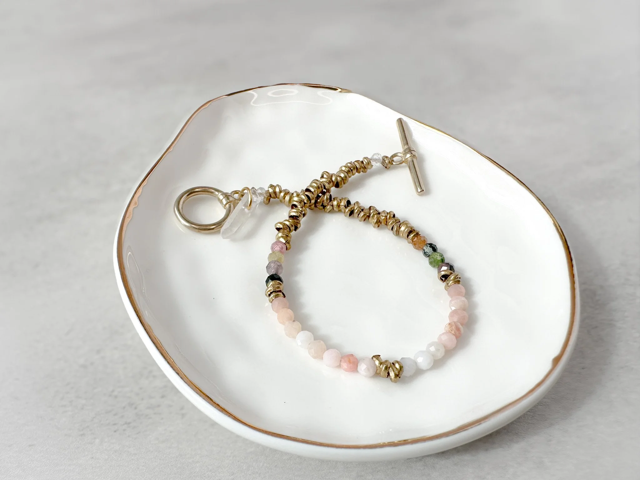 Aurora bracelet on dish with brass toggle clasp and clear quartz charm detail