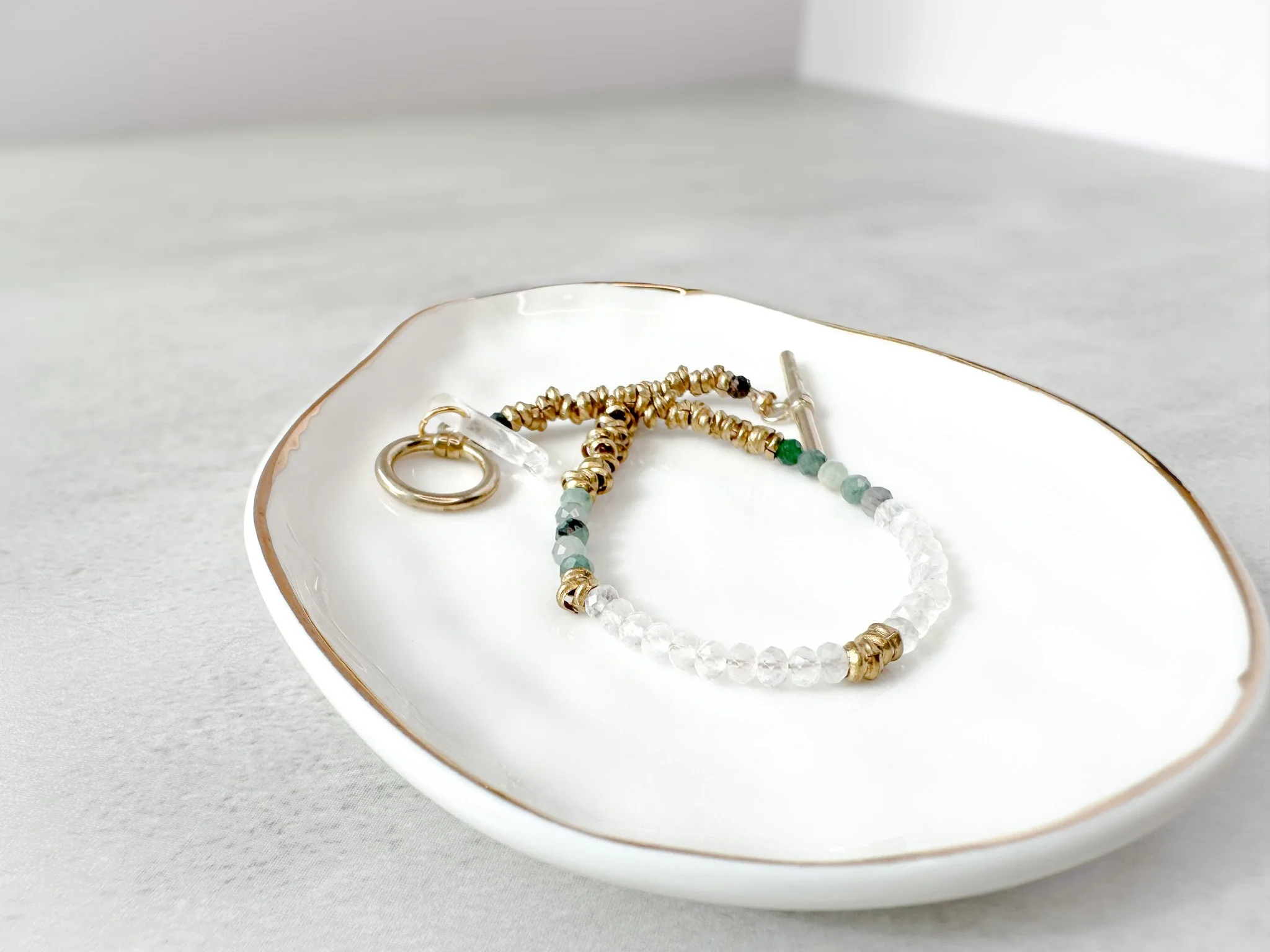 Vesper bracelet on dish with brass toggle clasp and clear quartz charm detail