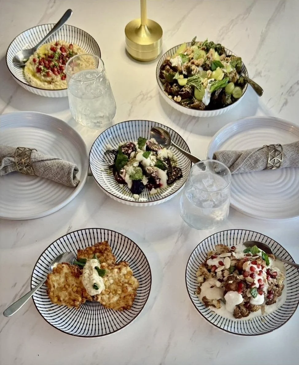A table set with assorted salads, fried food, and desserts, with water glasses, napkins, and a gold candle holder.