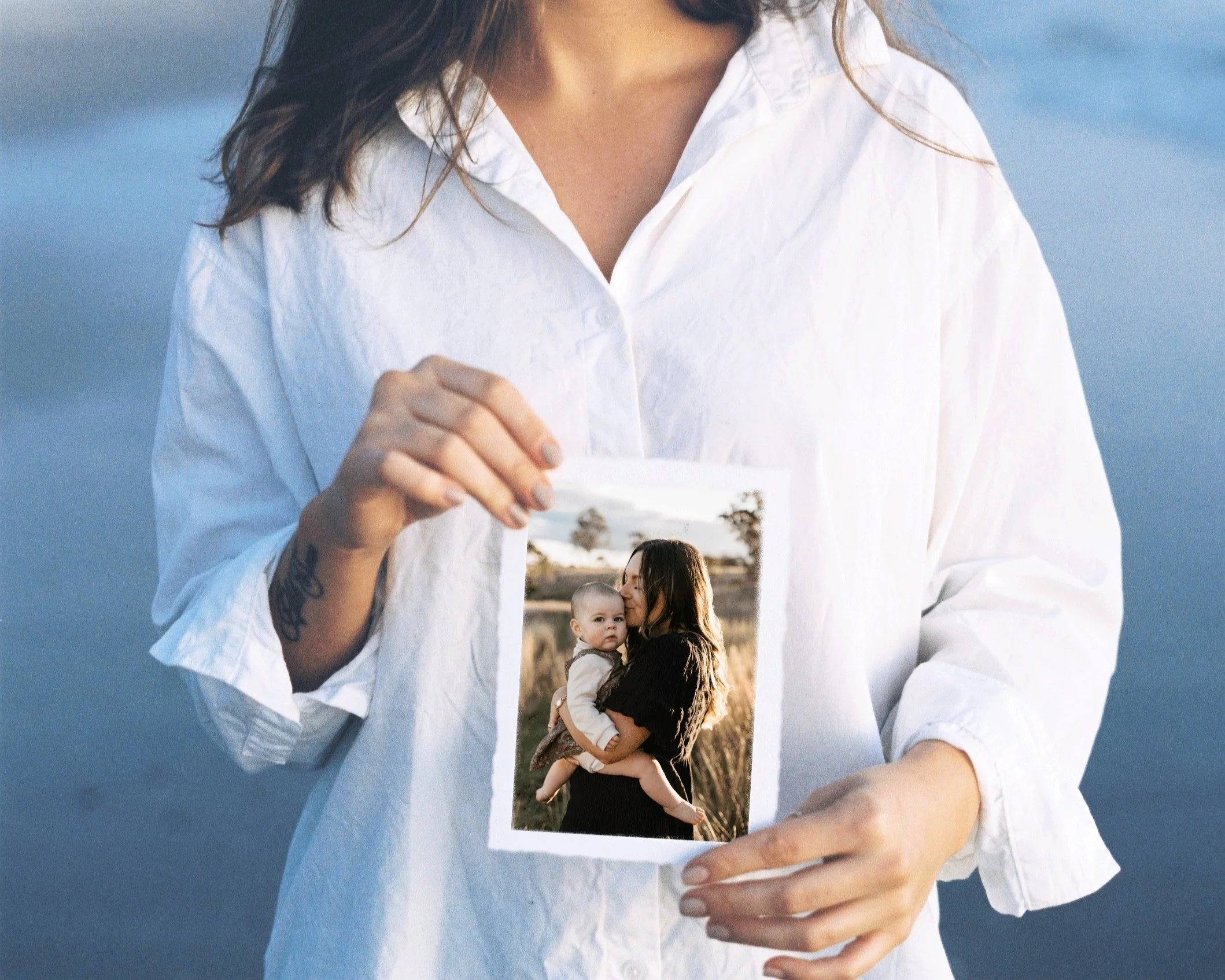 A person in a white shirt holding a photo of a woman hugging a baby outdoors.