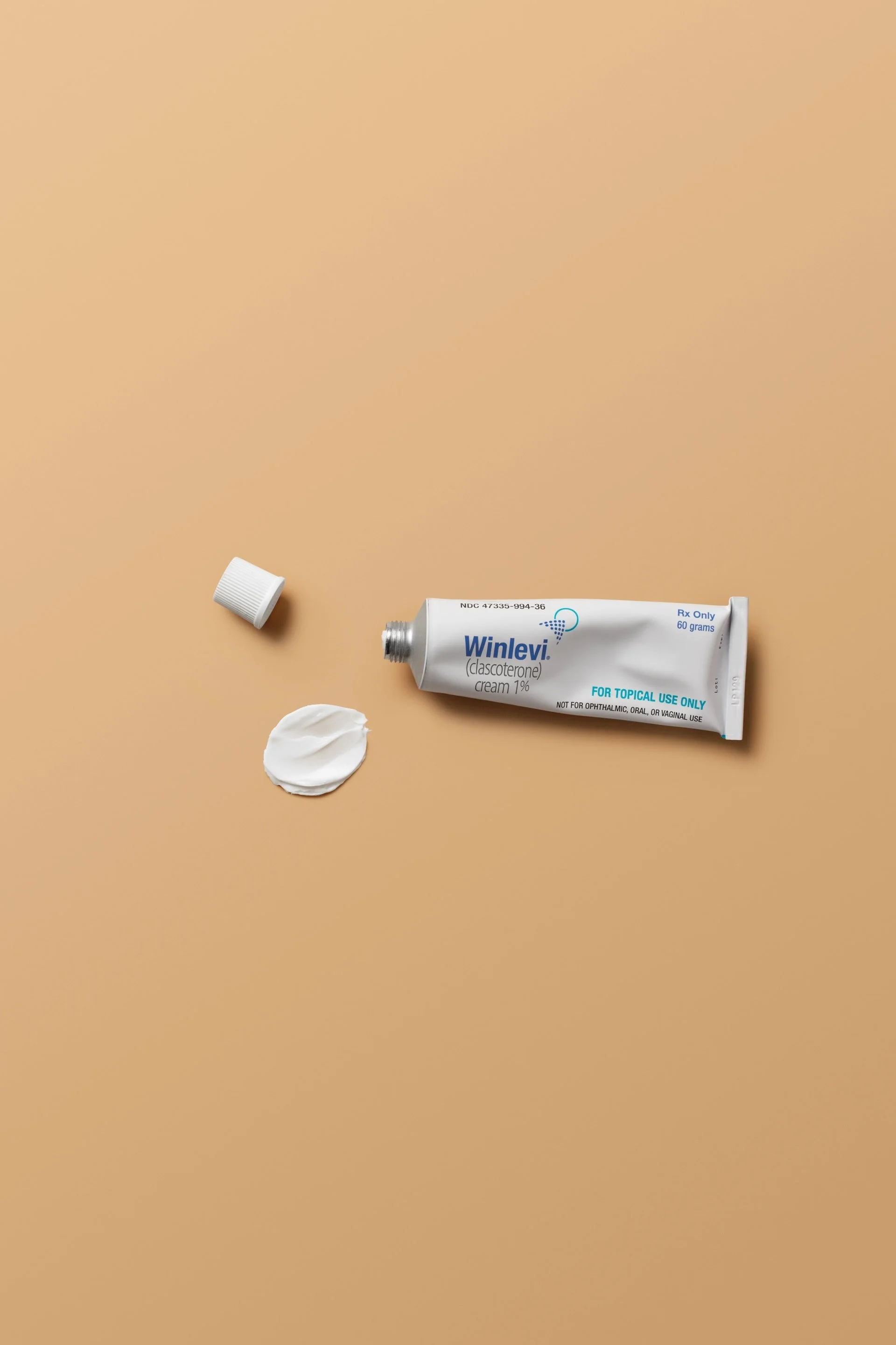 Tube of Winlevi cream with an open cap and a smear of cream on a brown background.