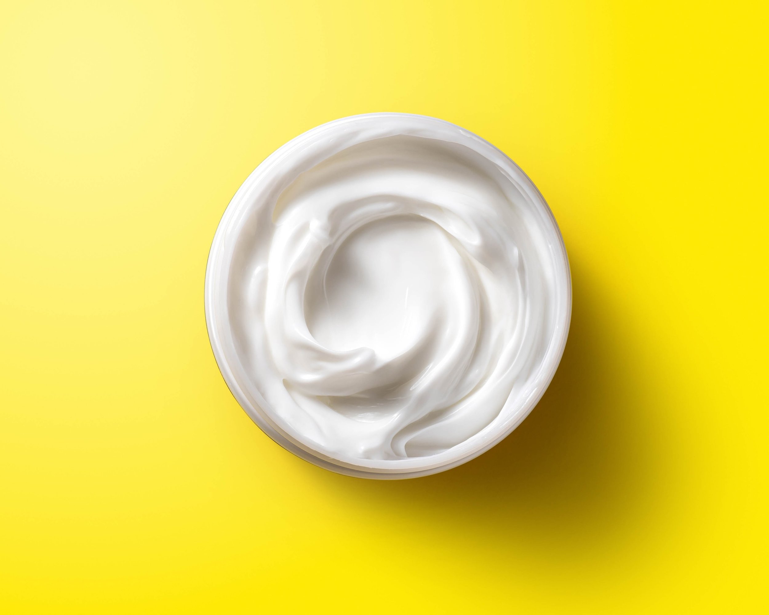Open jar of white cream on a yellow background