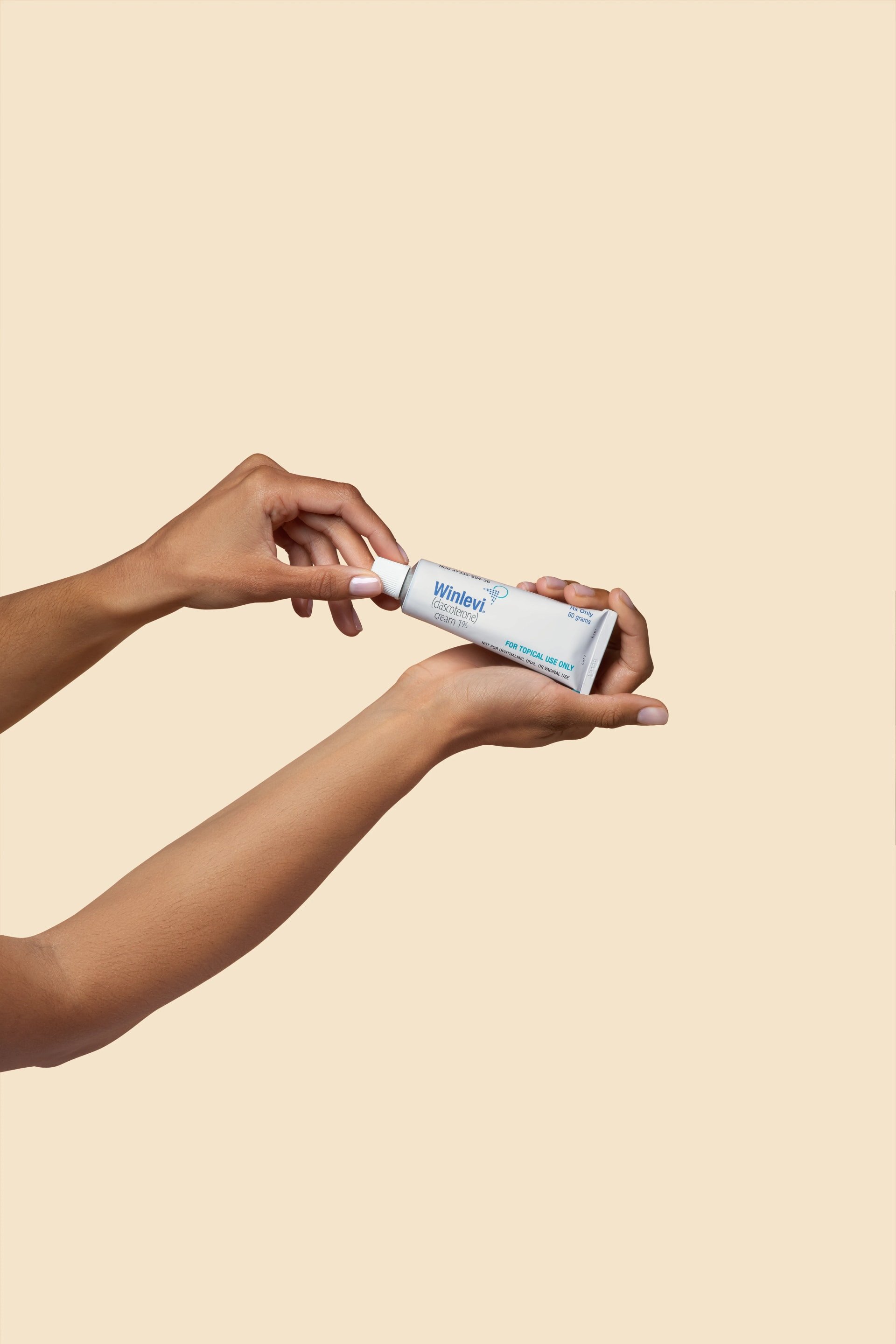 Hands holding a tube of Winlevi cream against a beige background.