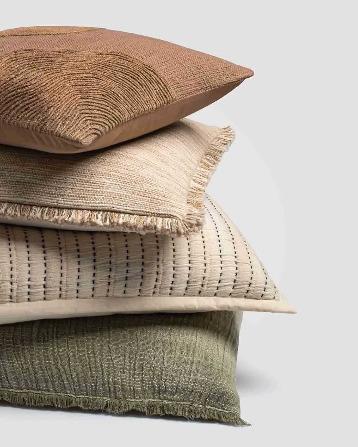 A neatly stacked pile of four decorative throw pillows in neutral tones with textured and patterned fabrics.