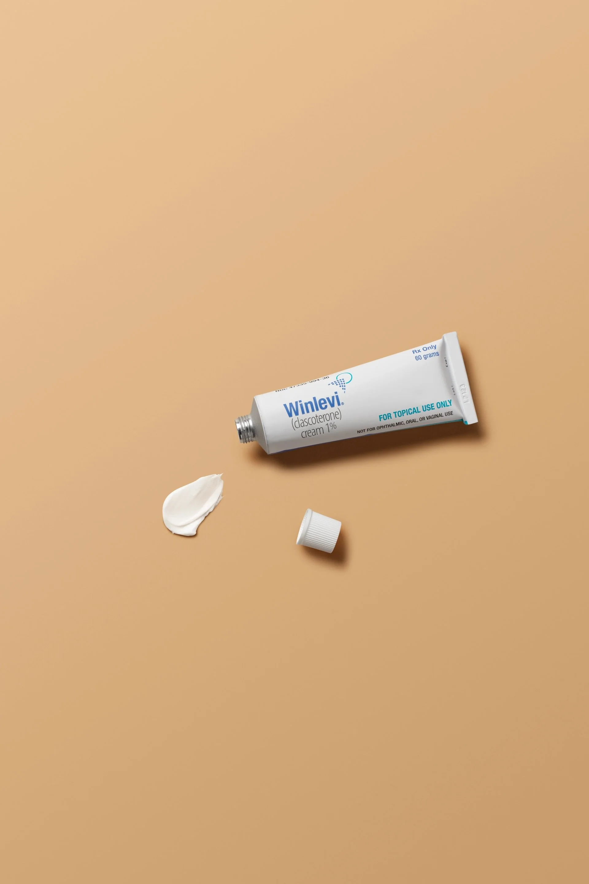 Open tube of Winlevi cream with cap and cream spot on beige background.