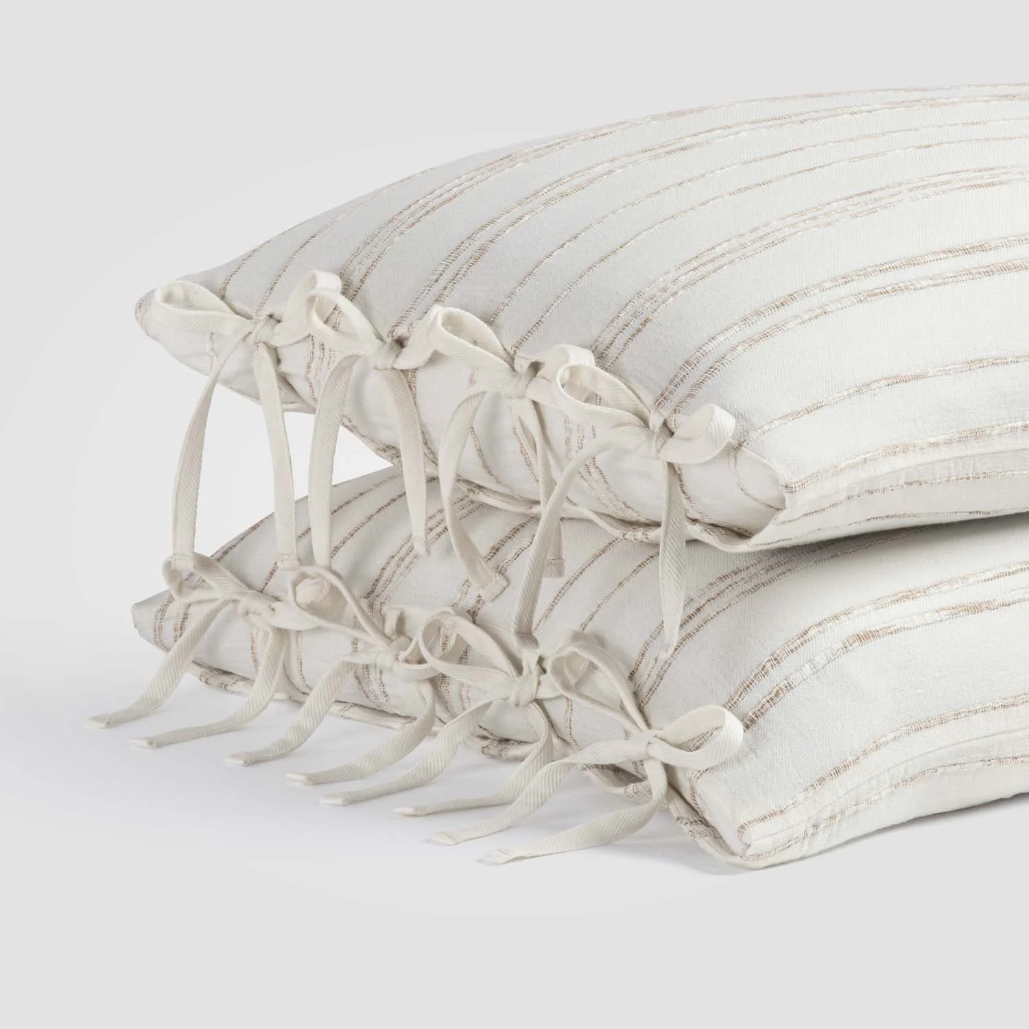 Two stacked cream-colored decorative pillows with striped patterns and tied bows on the edges.