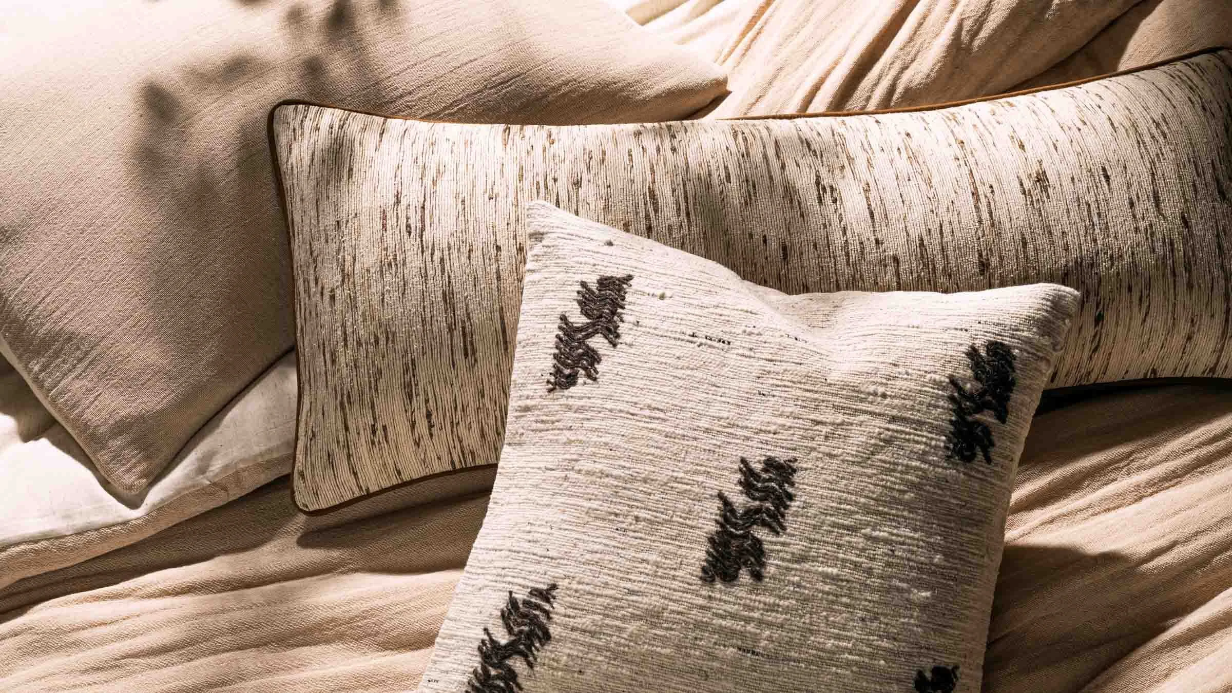 A collection of beige and cream-colored pillows with textured and embroidered patterns arranged on a bed.
